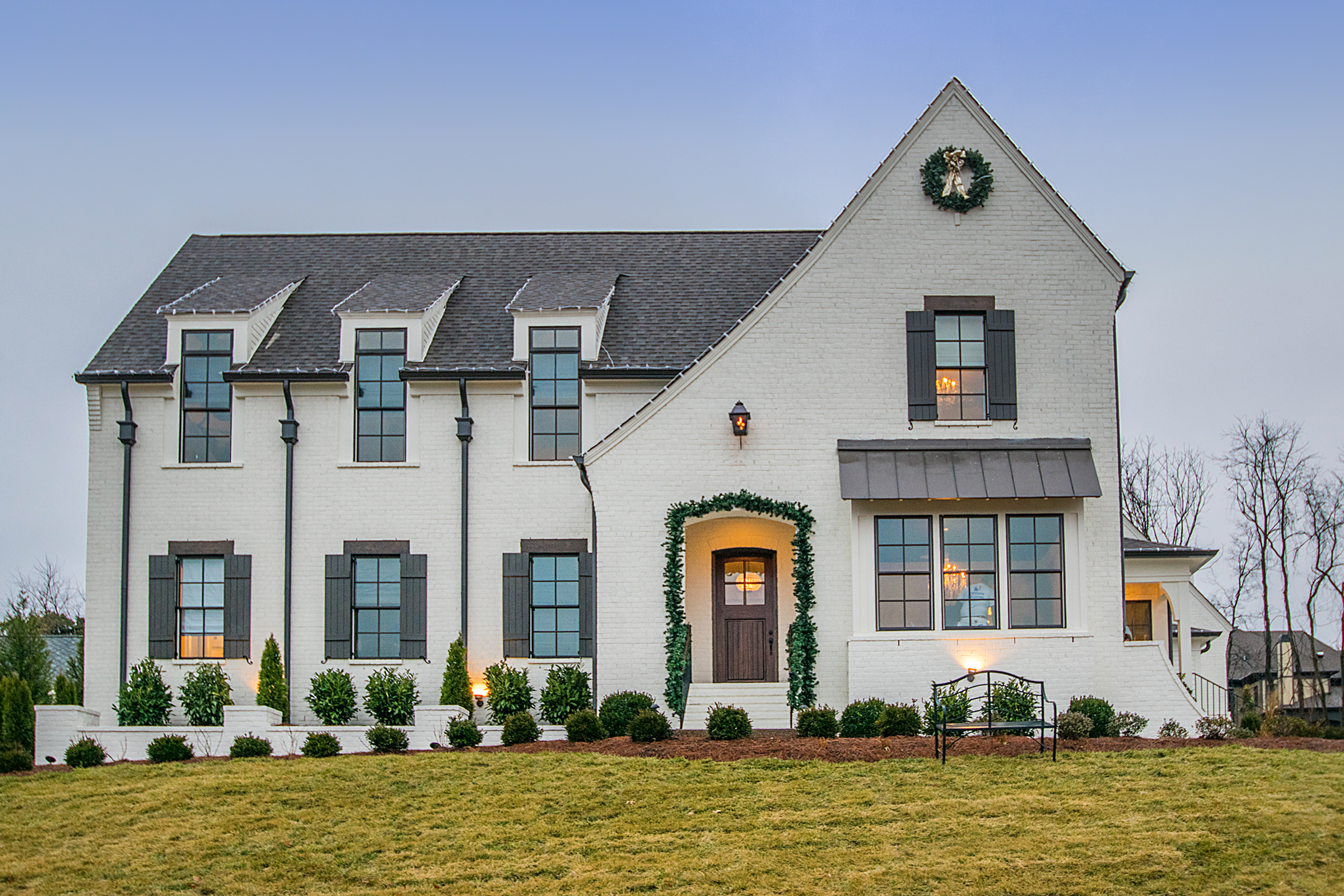 White two-story home with dark roof, and an asymmetrical gable and roofline with arched front door entry