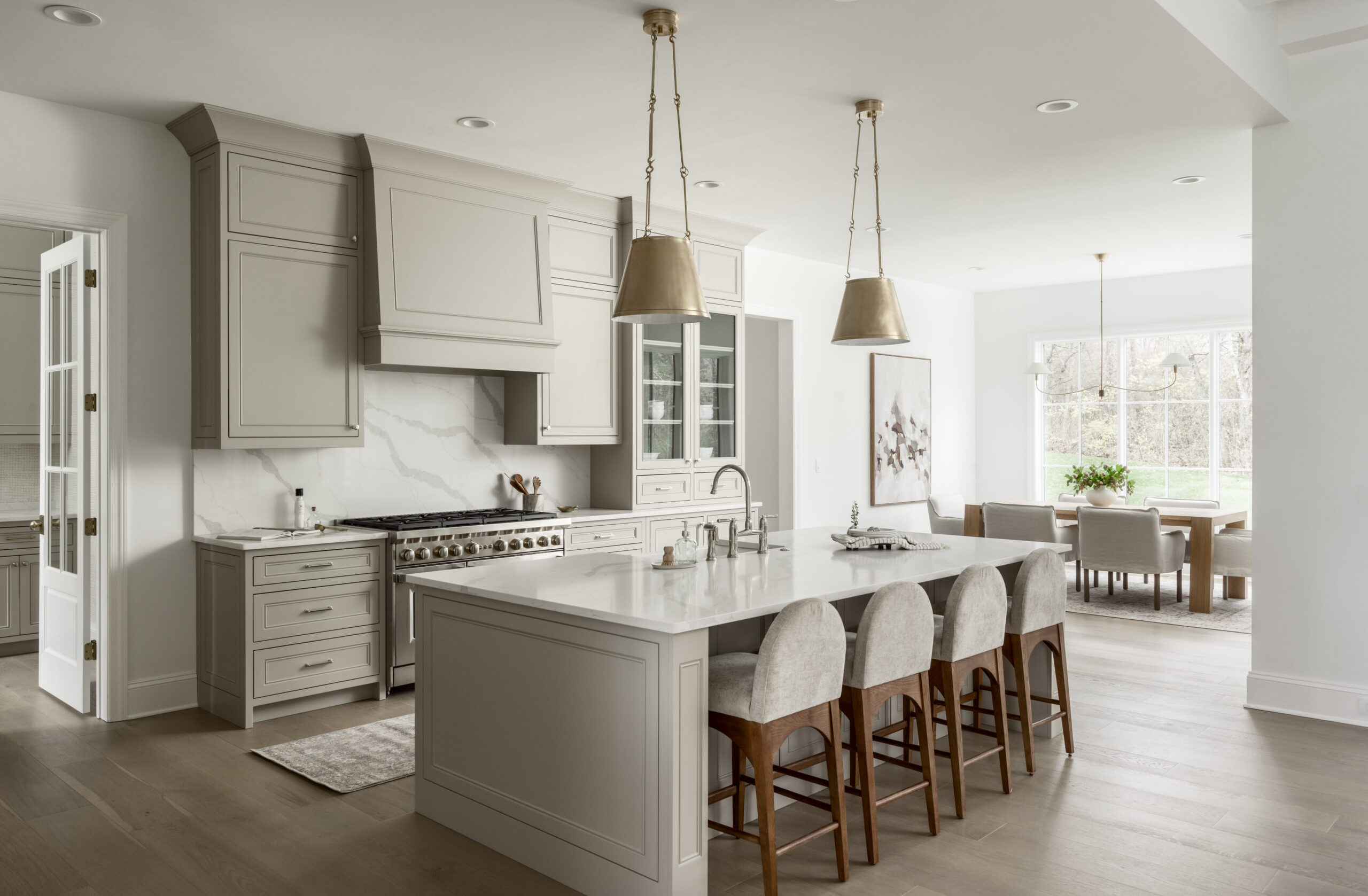 Kitchen with light gray cabinets and white countertops with range and hood and an island with brushed gold pendant lights