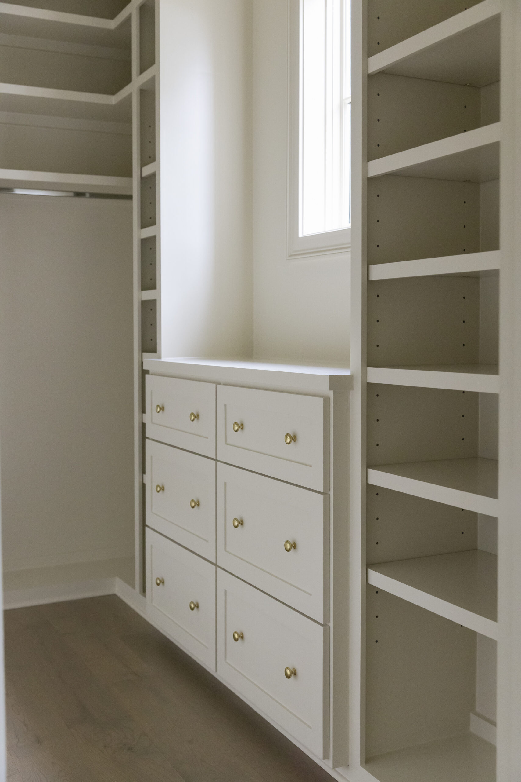 Creamy white walk-in closet with both open shelving and drawers for added storage.