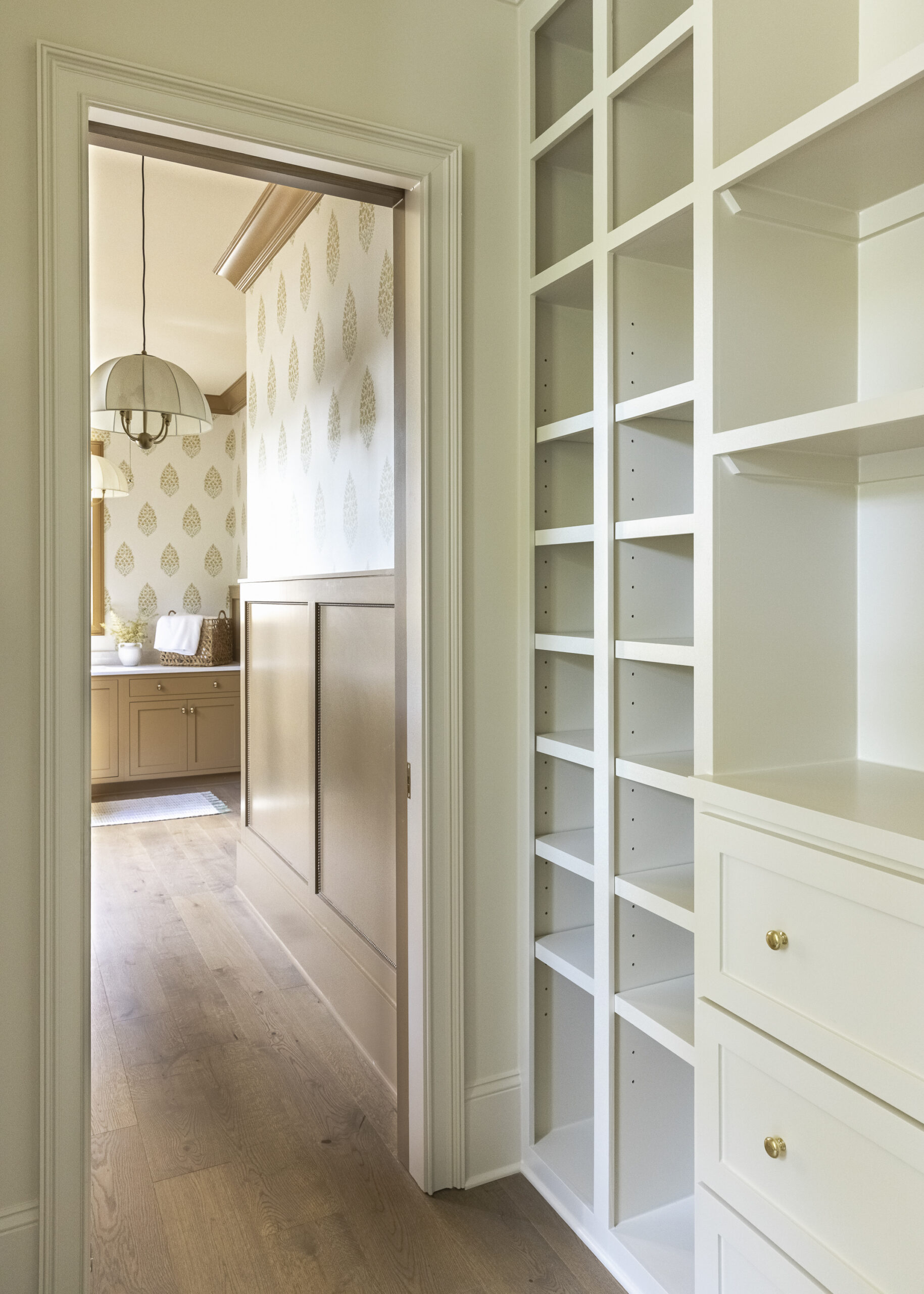 Large walk-in closet with creamy built-ins with open shelving and drawer storage near the laundry room.