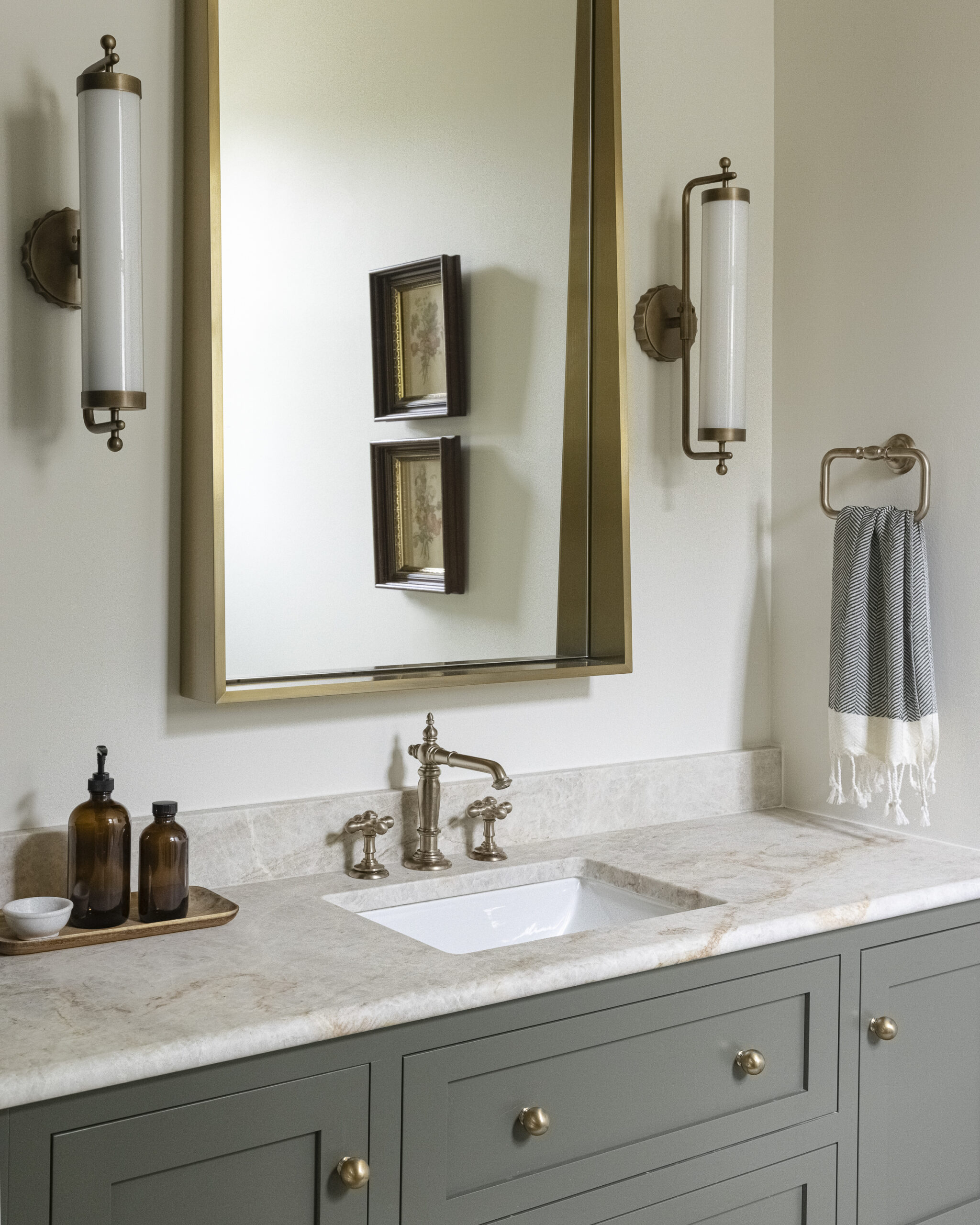 Muted green floating vanity and tan patterned tile and brushed gold mirror with white glass sconces