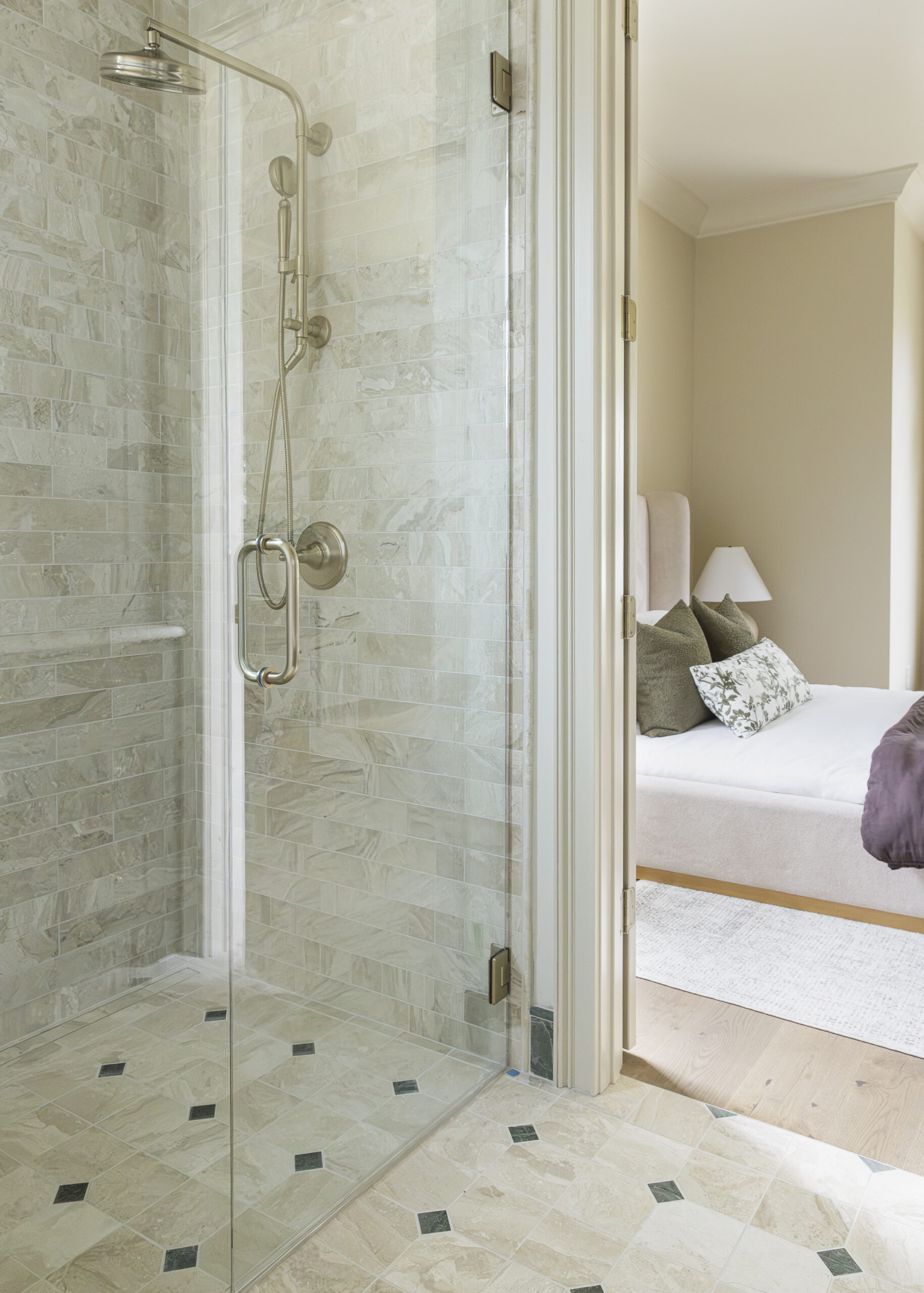 Glass front walk-in shower with patterned tile floor and a view of the bedroom
