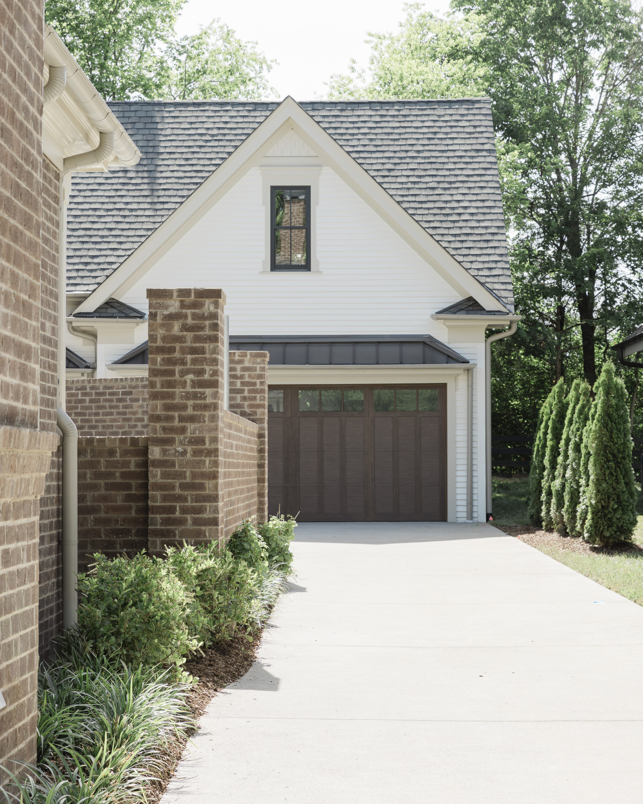 Driveway leading to a white siding attached garage with wood stained garage doors