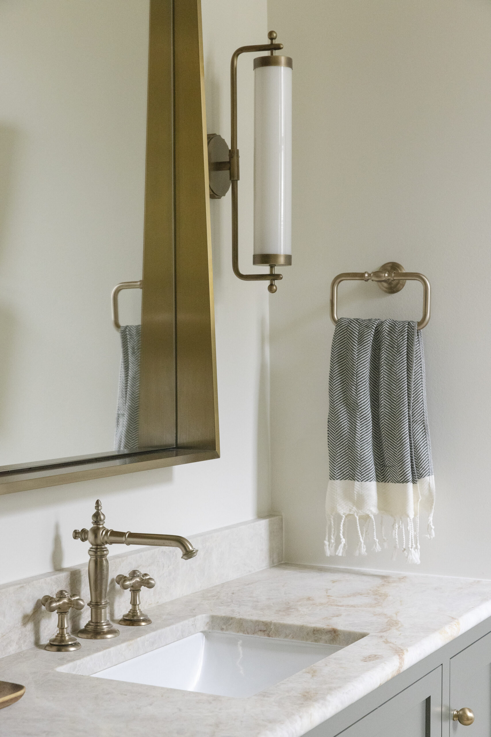 Muted green floating vanity and tan patterned tile and brushed gold mirror with white glass sconces