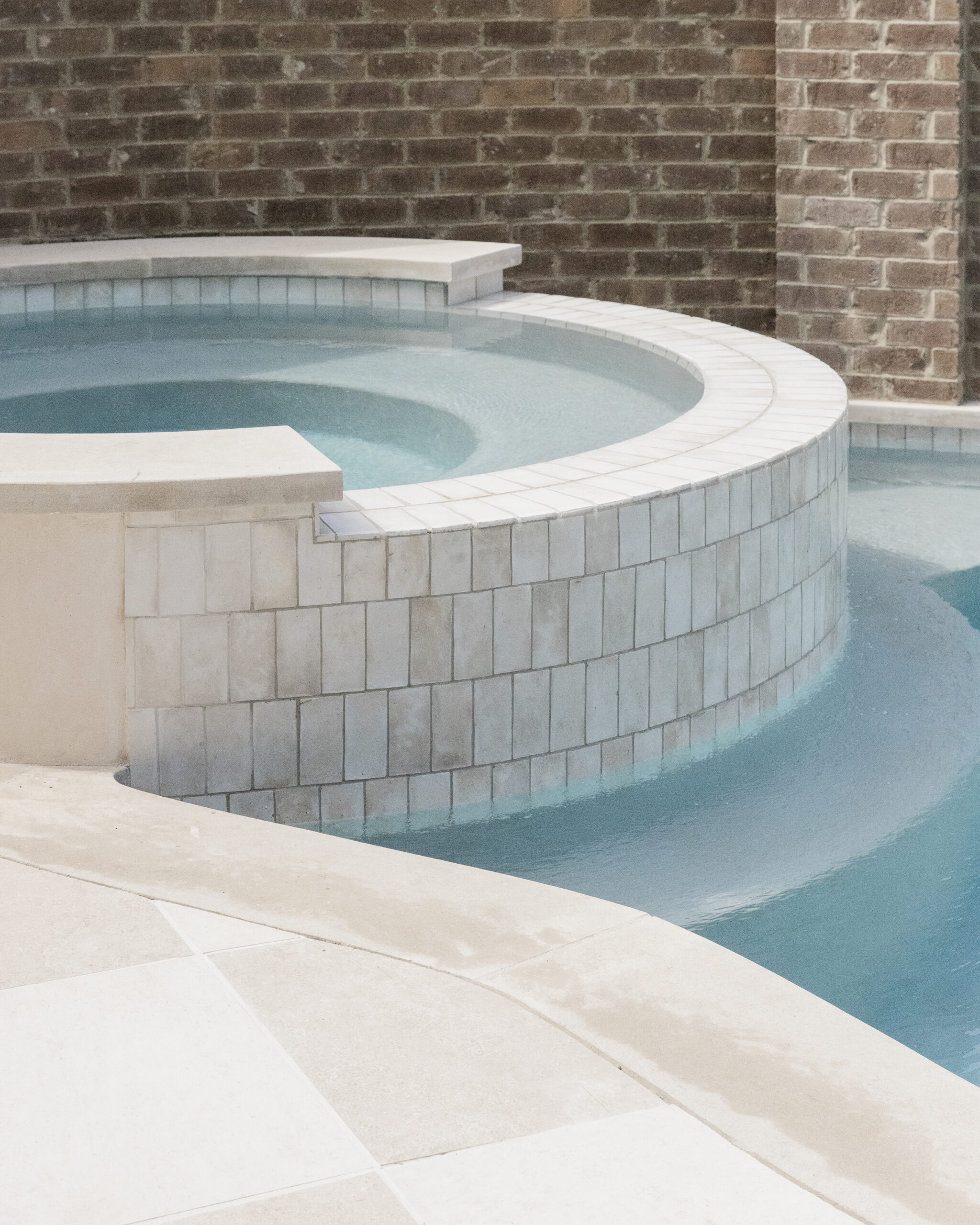 Circular hot tub with light tile siding beside plunge pool