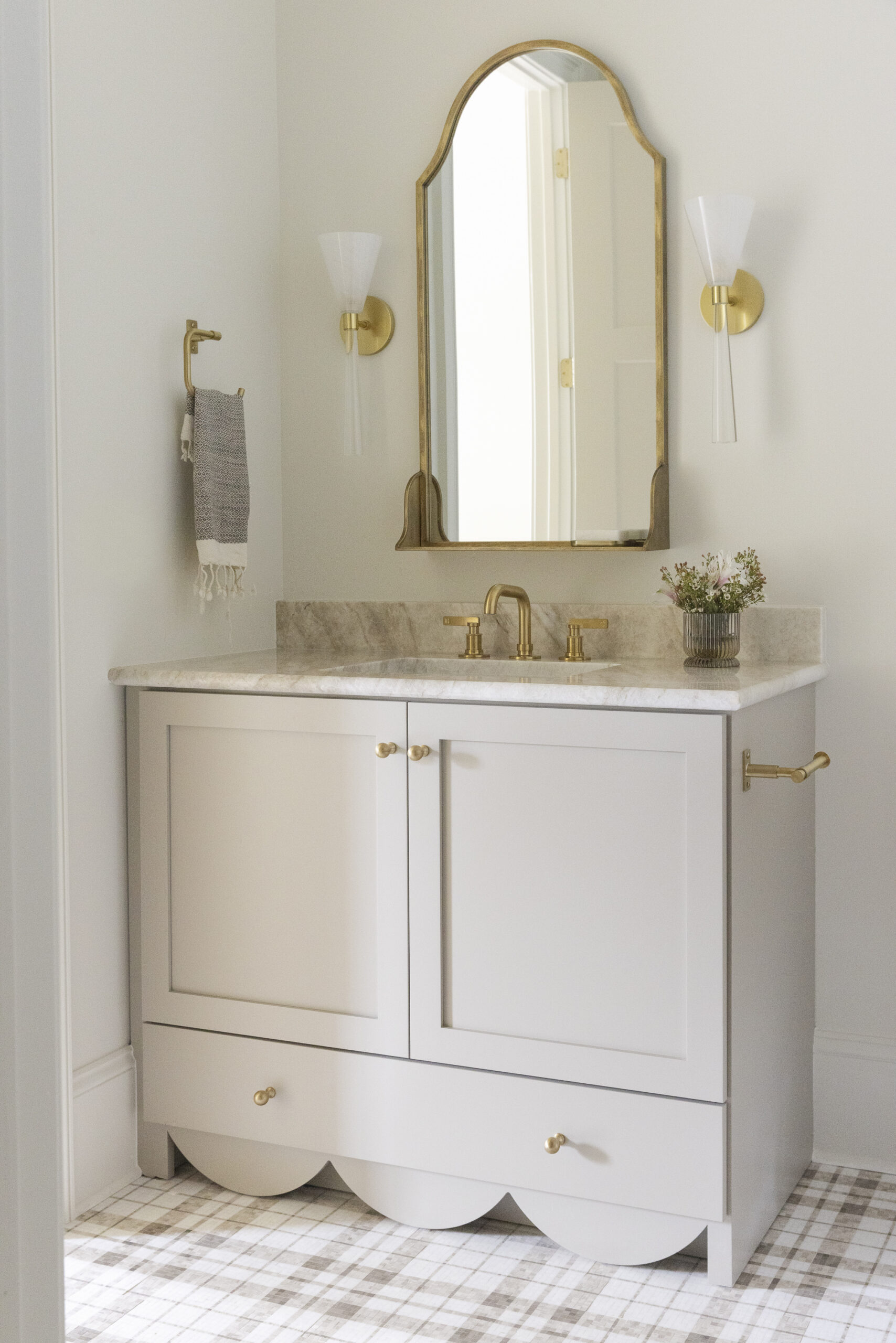 Taupe vanity with scalloped base, brown and white checkered tile, an arched mirror and sconces