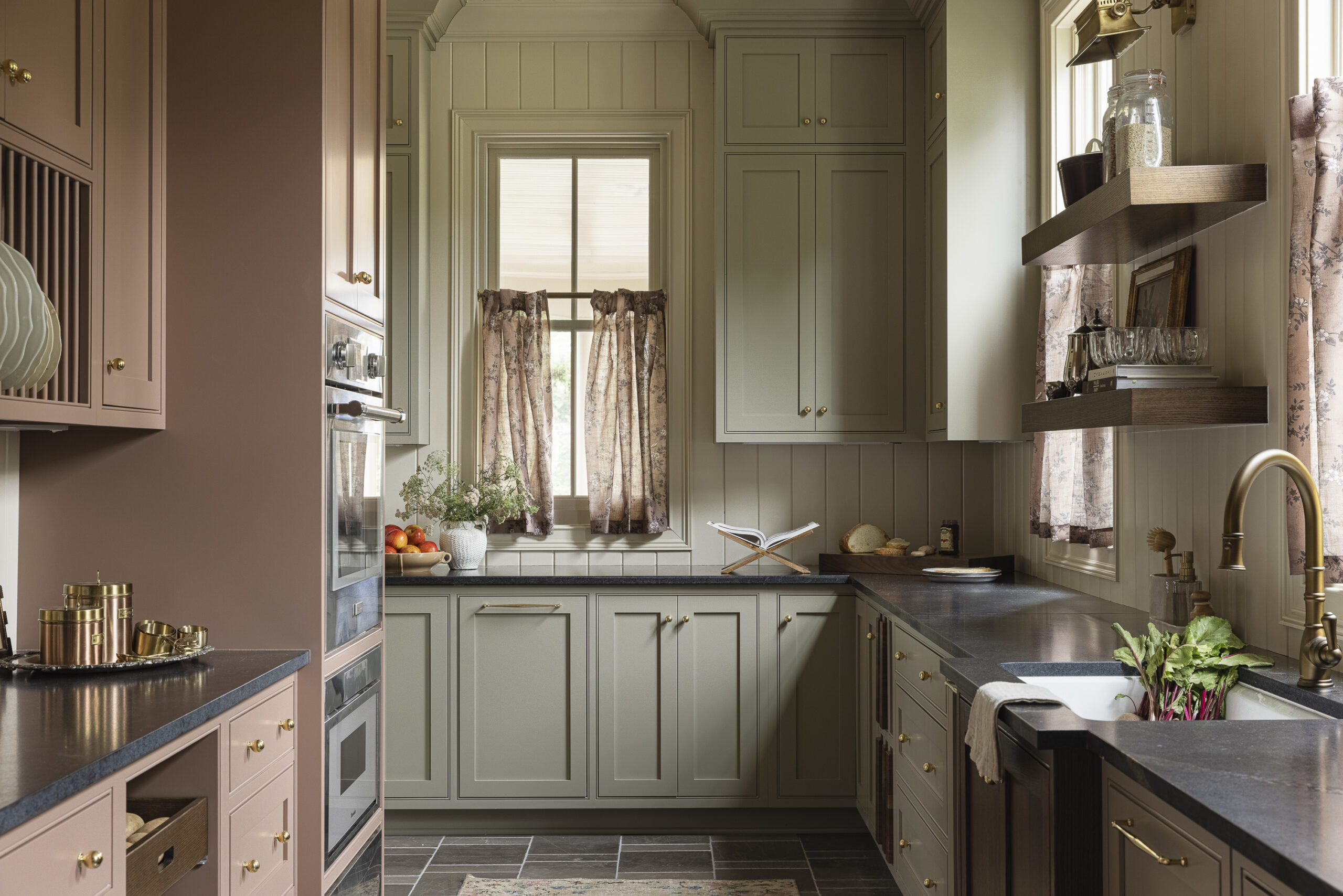 Scullery with sage cabinets, black soapstone cabinets and v-groove cream wall paneling and window with decorative brass wall sconces
