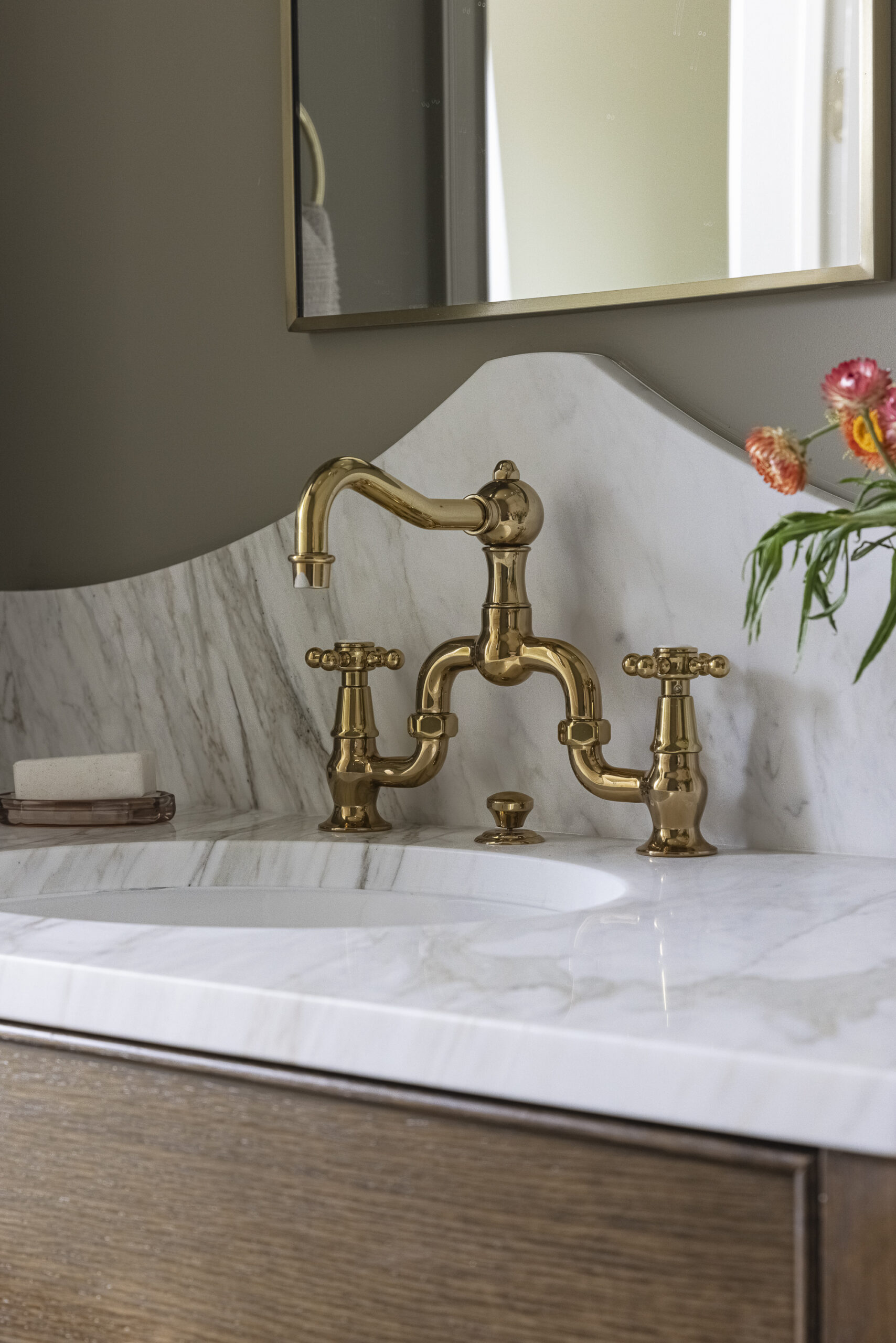 Bathroom with wood stained vanity, marble countertop with brushed gold fixtures a mirror and sconces