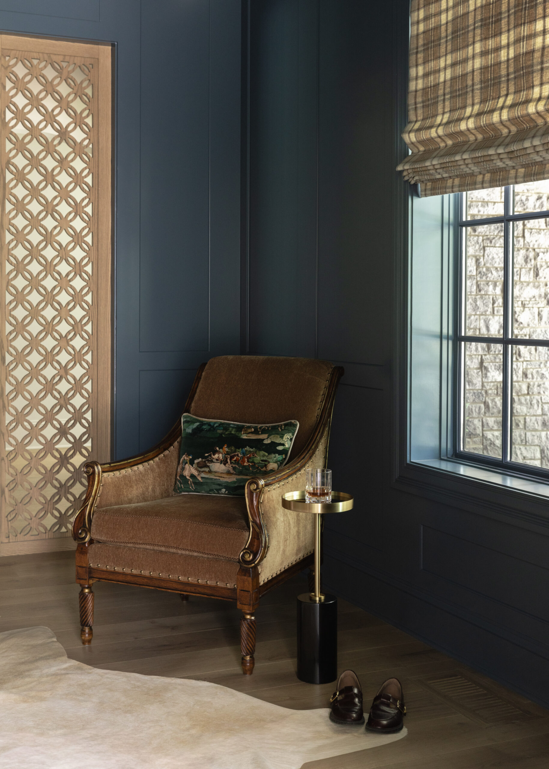 Deep navy walls with upholstered chair beside a window and carved wooden decorative panels