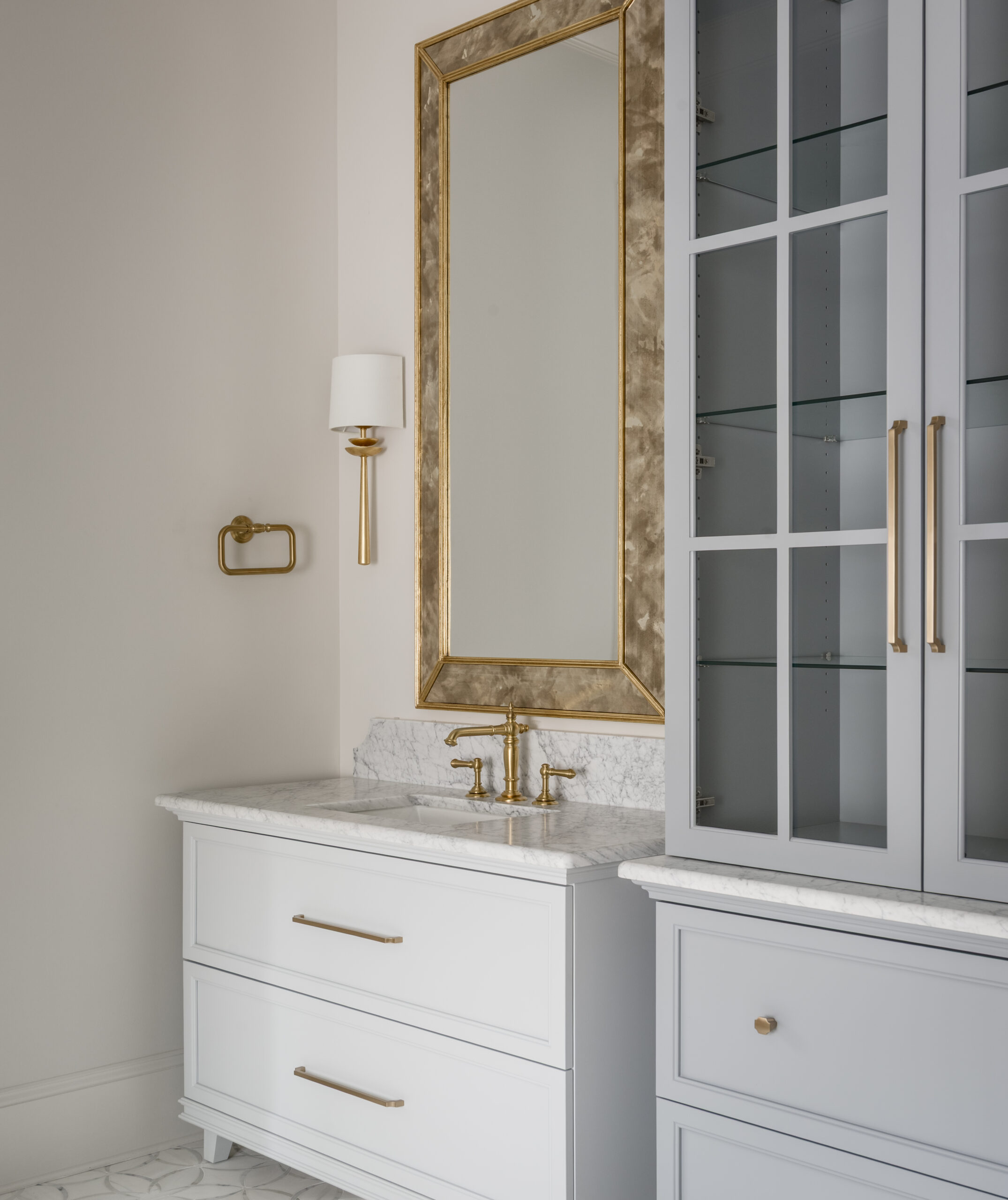Light gray dual vanities with paneled glass front powder blue linen furniture piece and gold mirrors and sconces