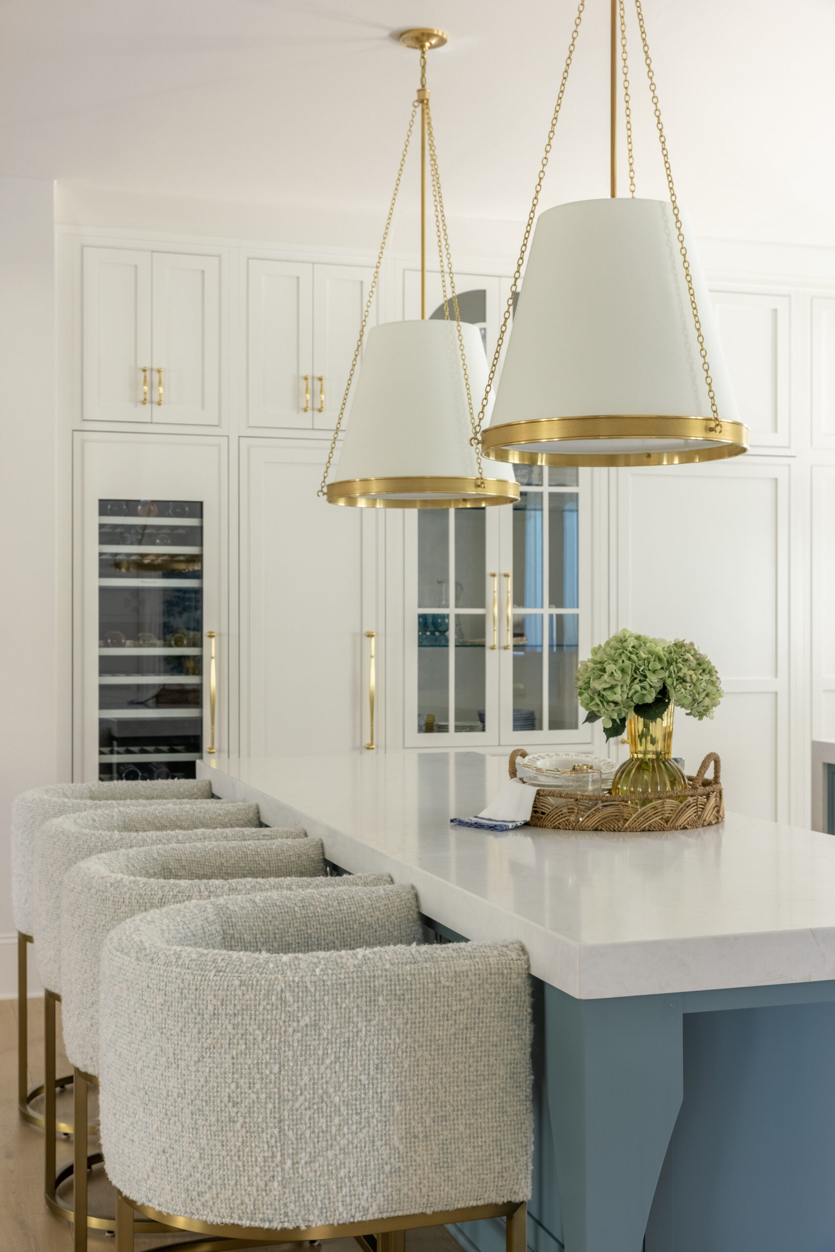Side view of kitchen with double blue kitchen island cabinets and white countertops with white shaded pendants and glass front pantry cabinet