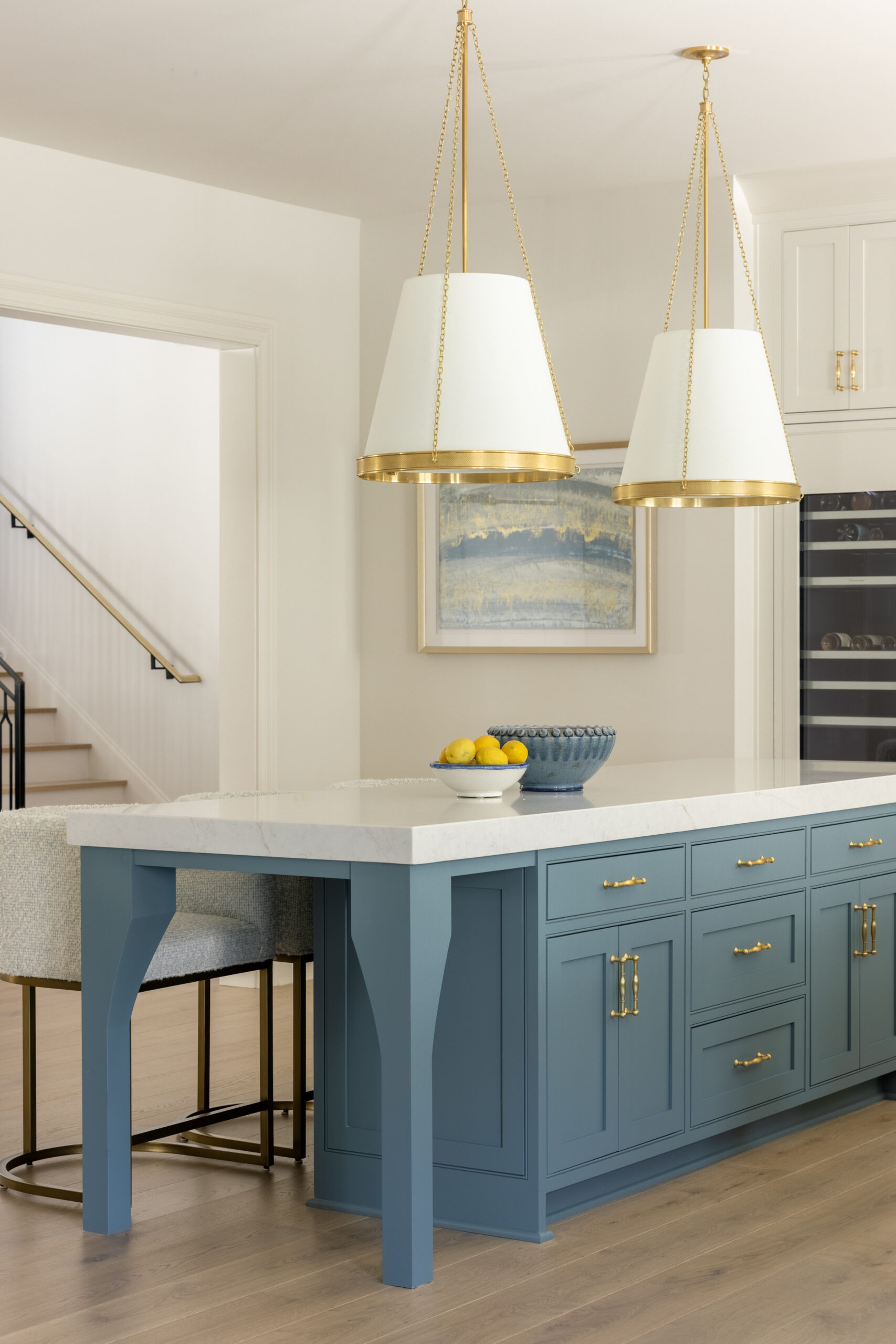Side view of kitchen with double blue kitchen island cabinets and white countertops with white shaded pendants and glass front pantry cabinet