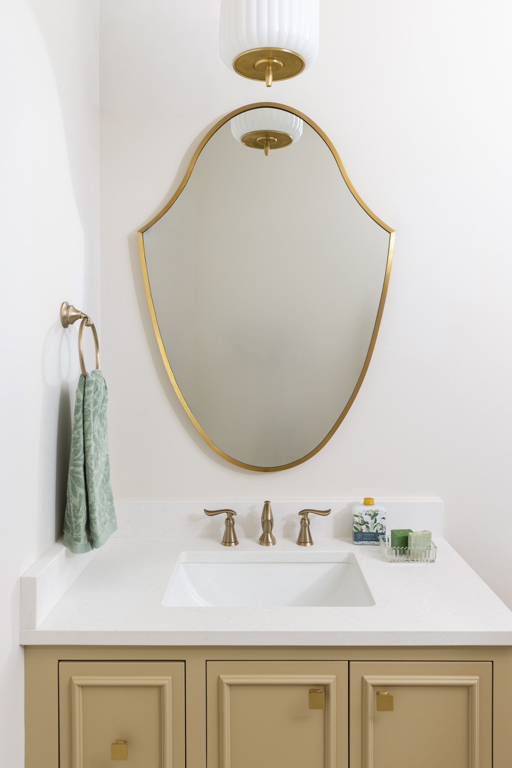 Yellow vanity with light countertops and a gold rimmed mirror with gold fixtures