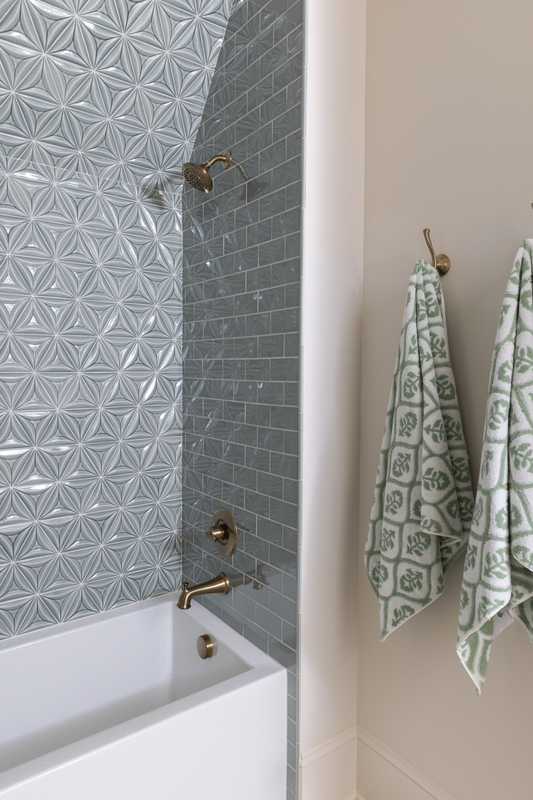 Blue subway tile with accent wall of blue tile and gold fixtures with towels hanging on wall hooks