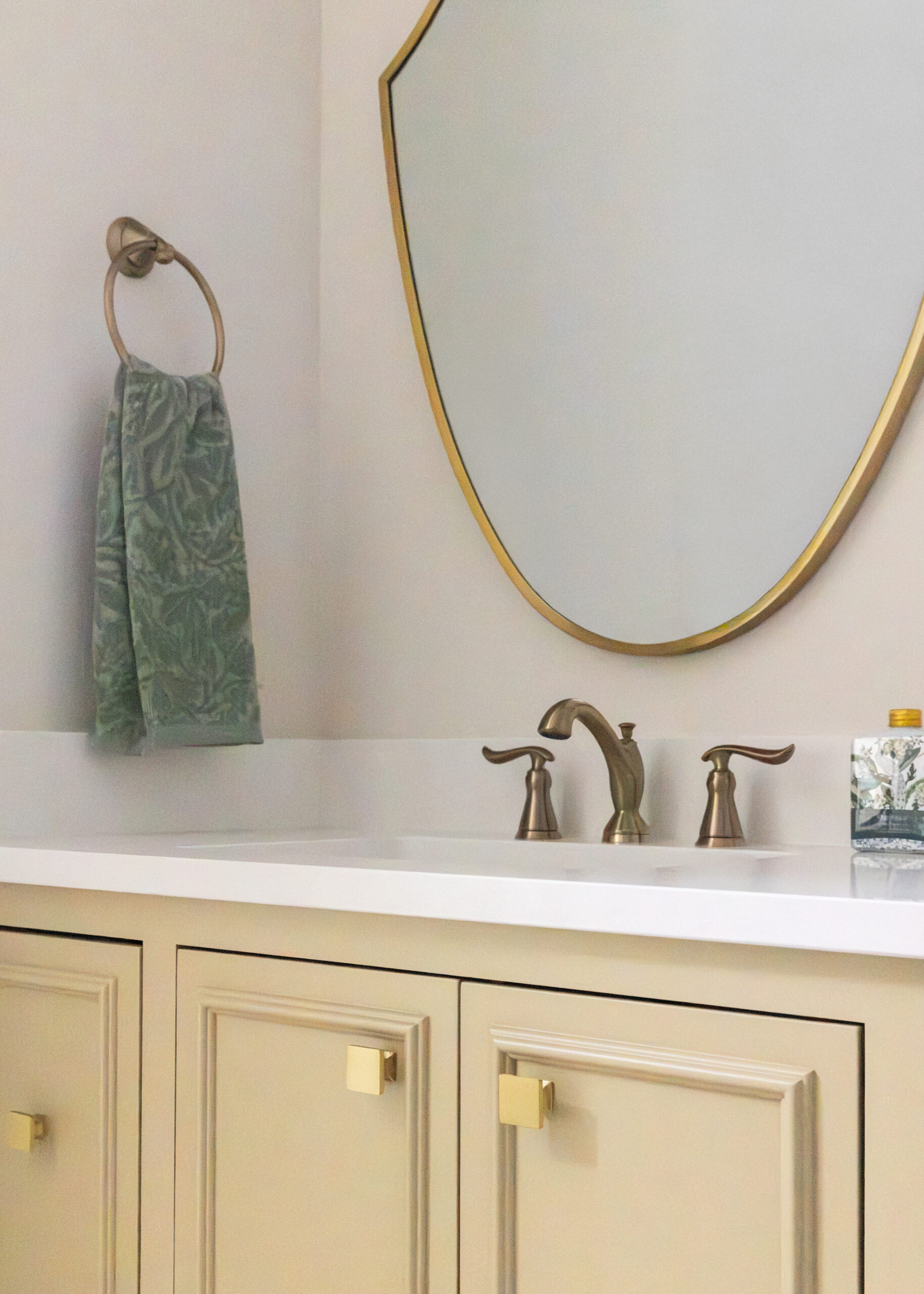 Yellow vanity with light countertops and a gold rimmed mirror with gold fixtures