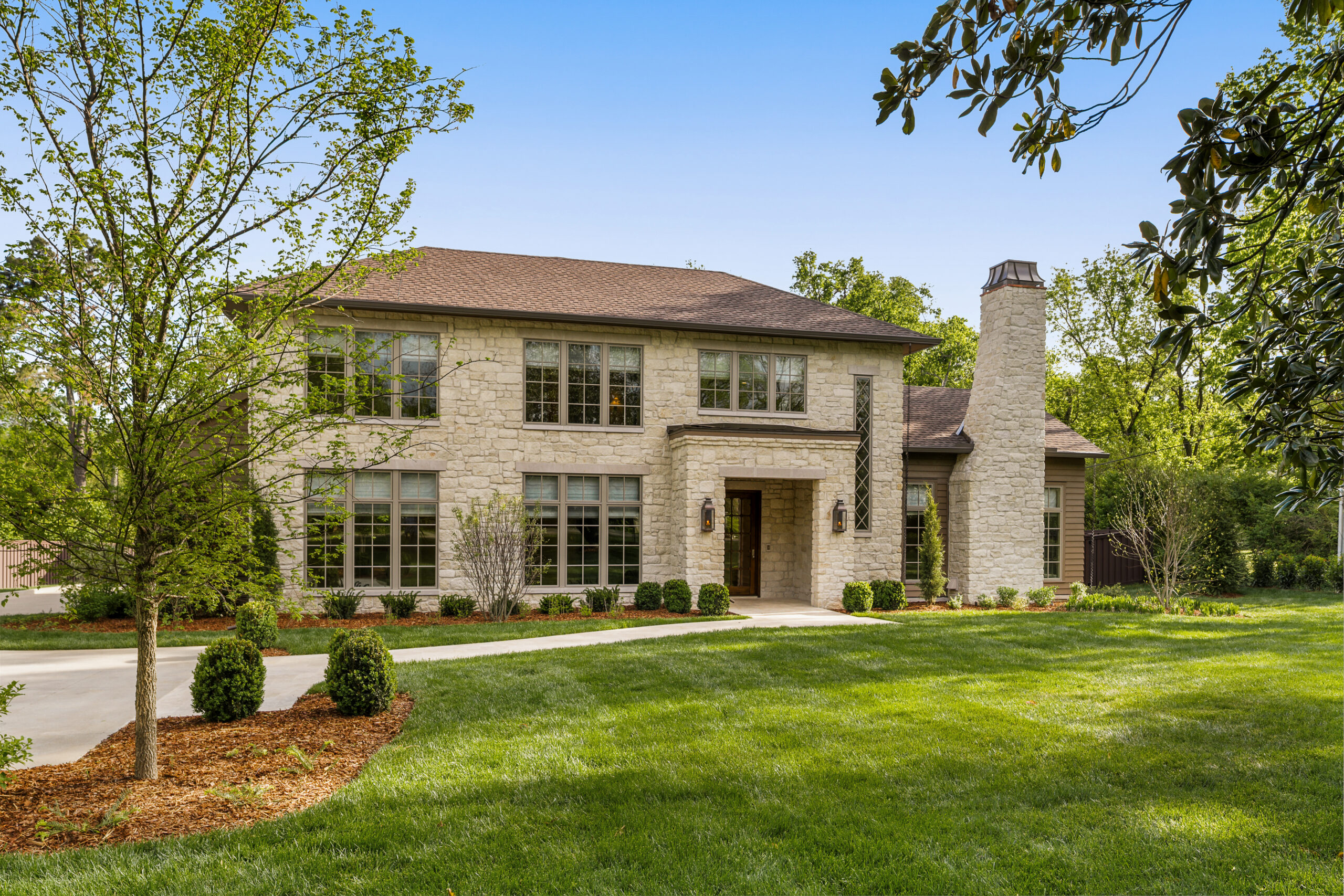 Spacious green lawn leading to a stone faced European style home with covered entrance and chimney