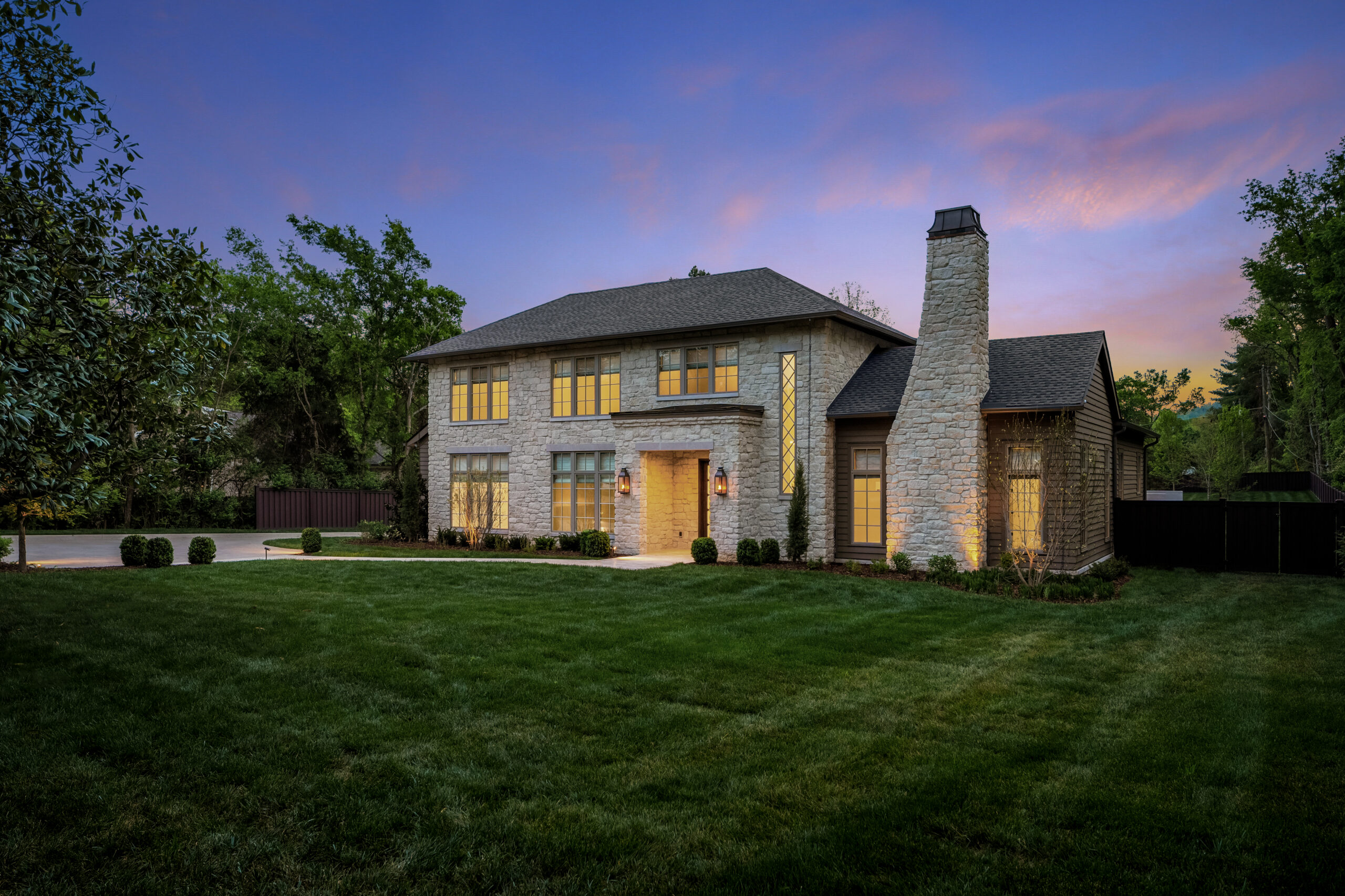 Spacious green lawn leading to a stone faced home with covered entrance and chimney