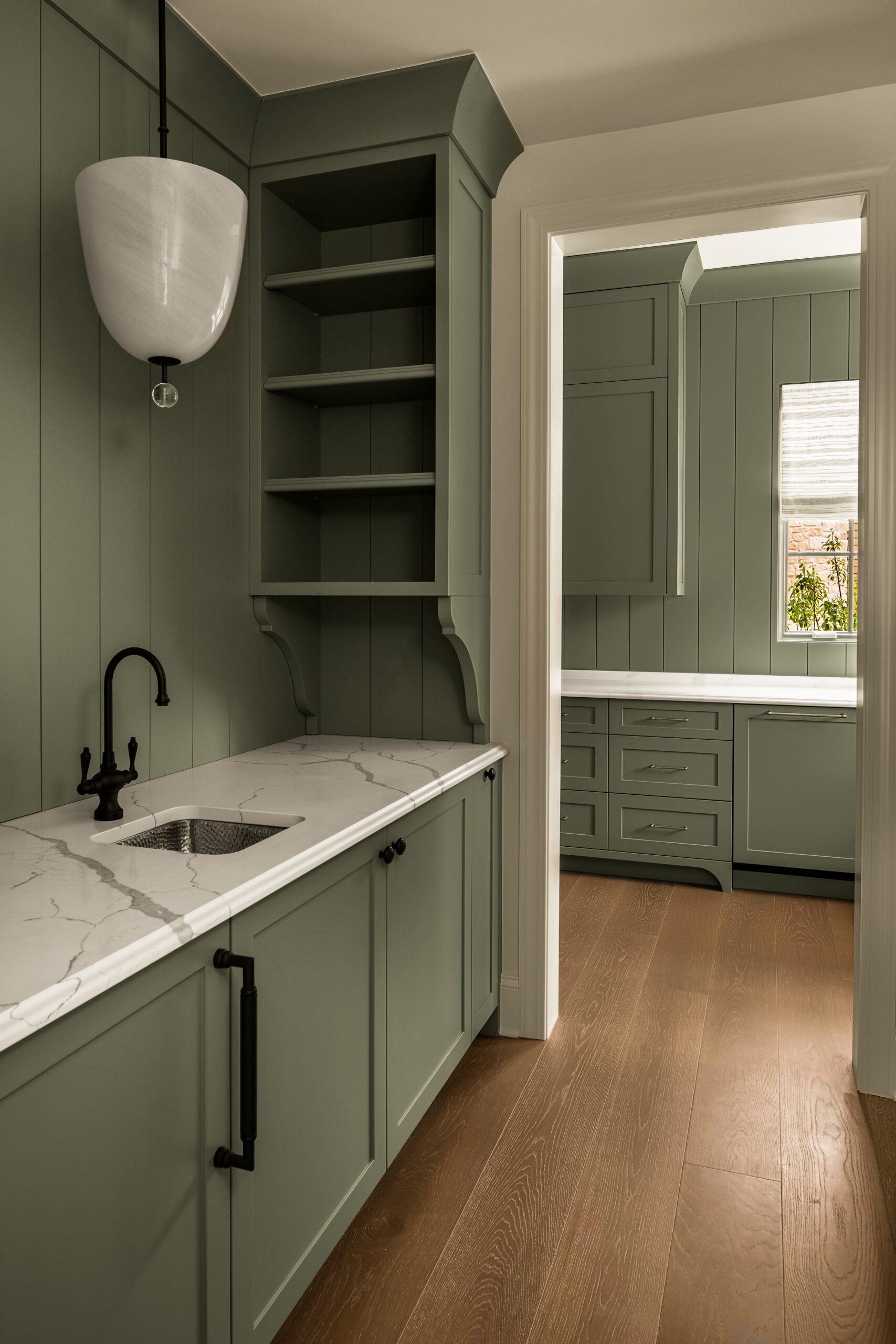 Muted sage green pantry cabinetry with paneled walls, light countertops, a utility sink and counter to ceiling open shelving