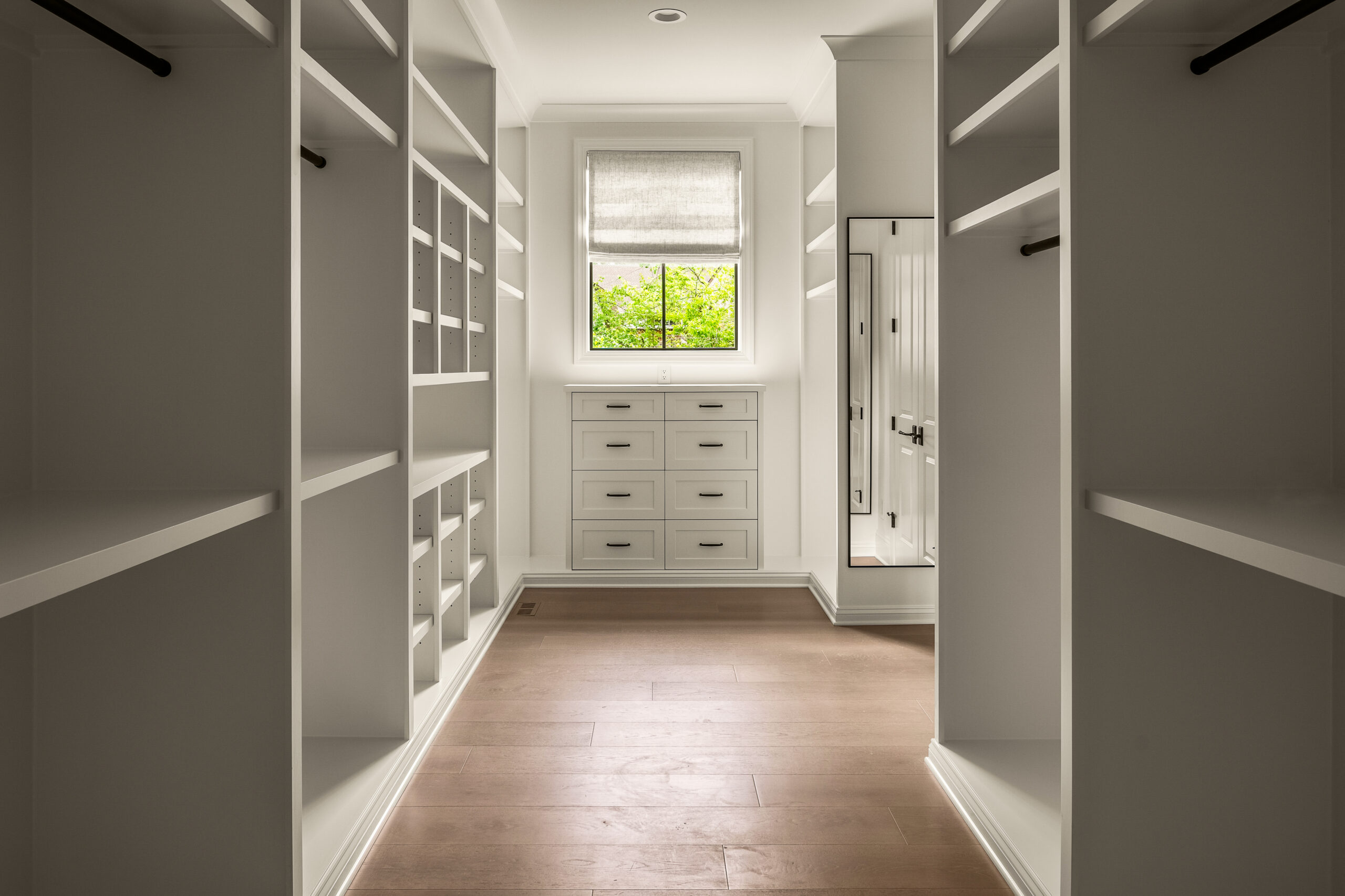 Large gray walk-in closet with open shelving, window light, and drawers for added storageunder window