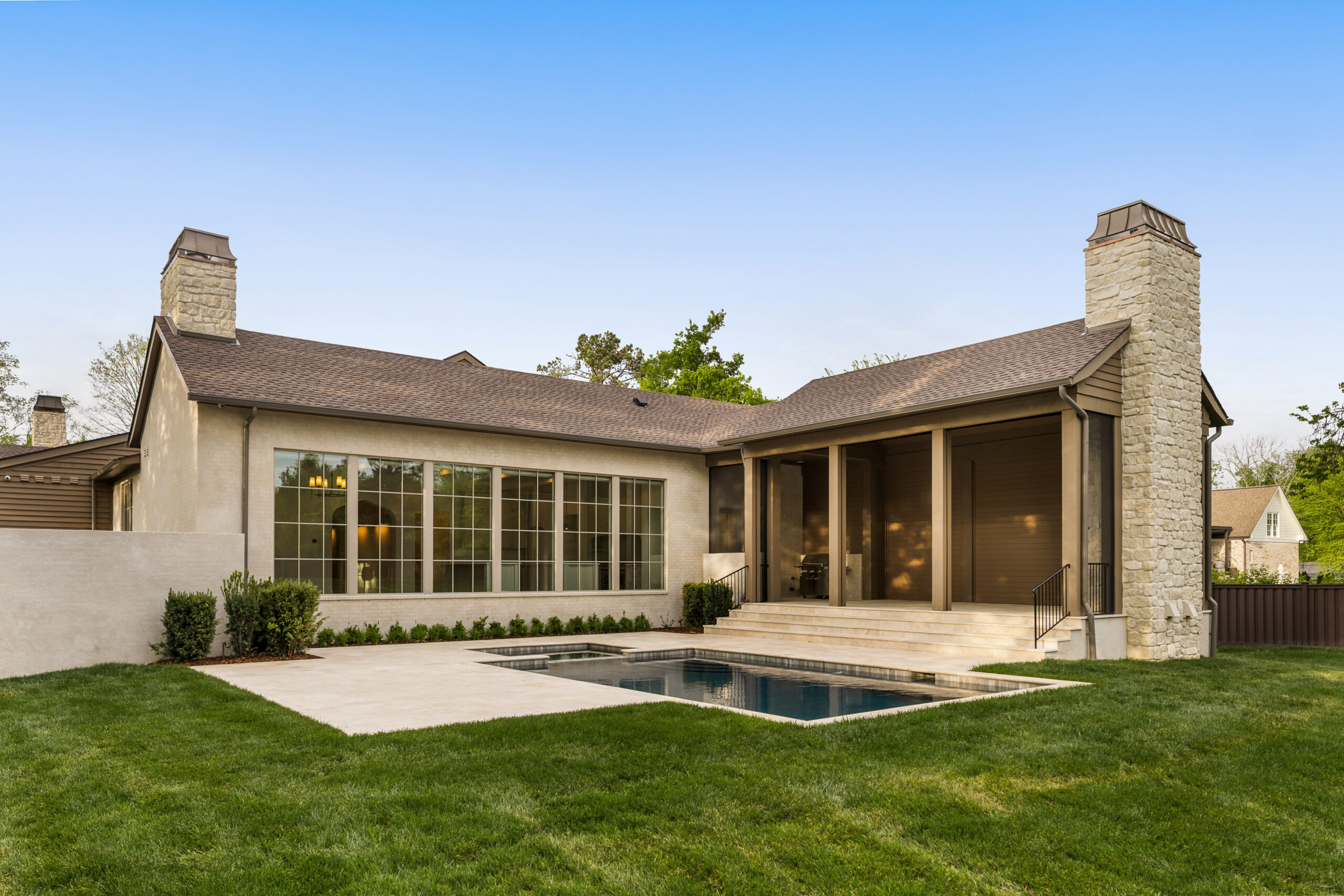 Covered back porch with tall ceiling, stone fireplace and chimney facing a swimming pool with concrete surround