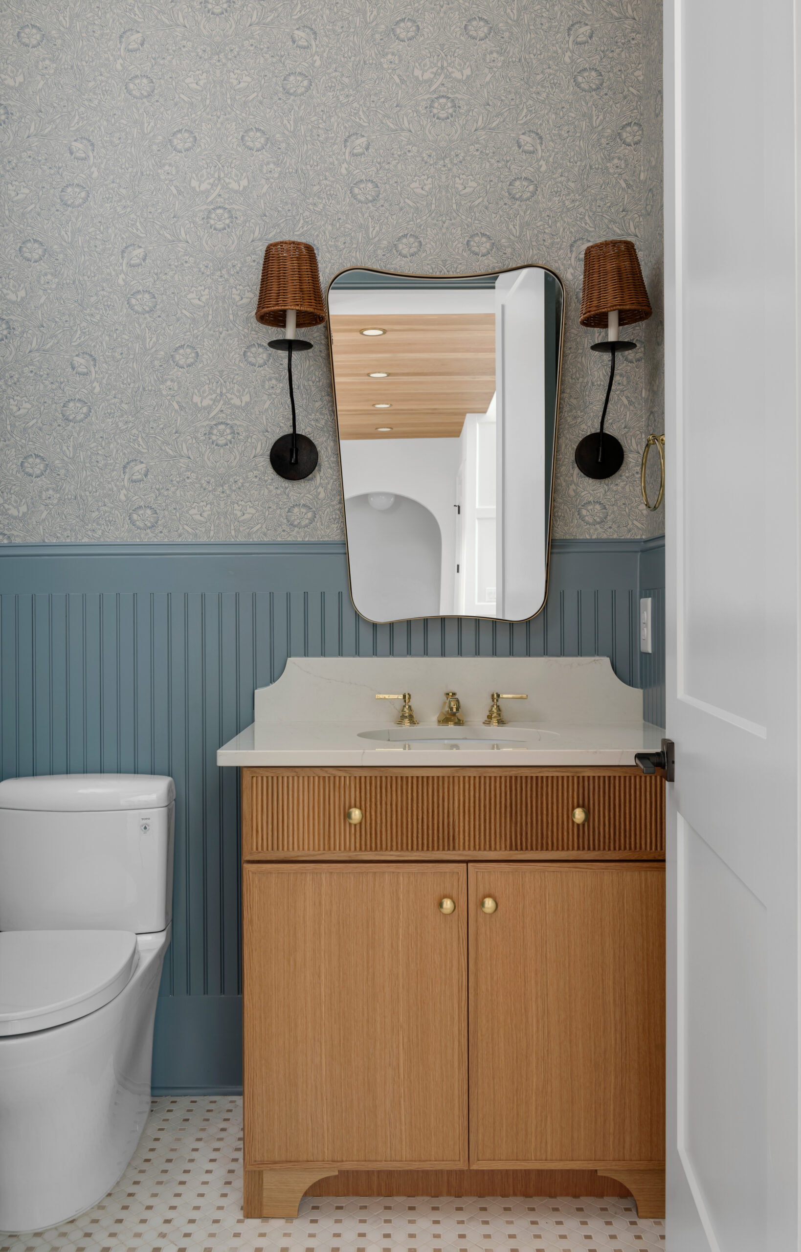 Single light wood vanity with powser blue paneled bathroom wall and wallpaper above