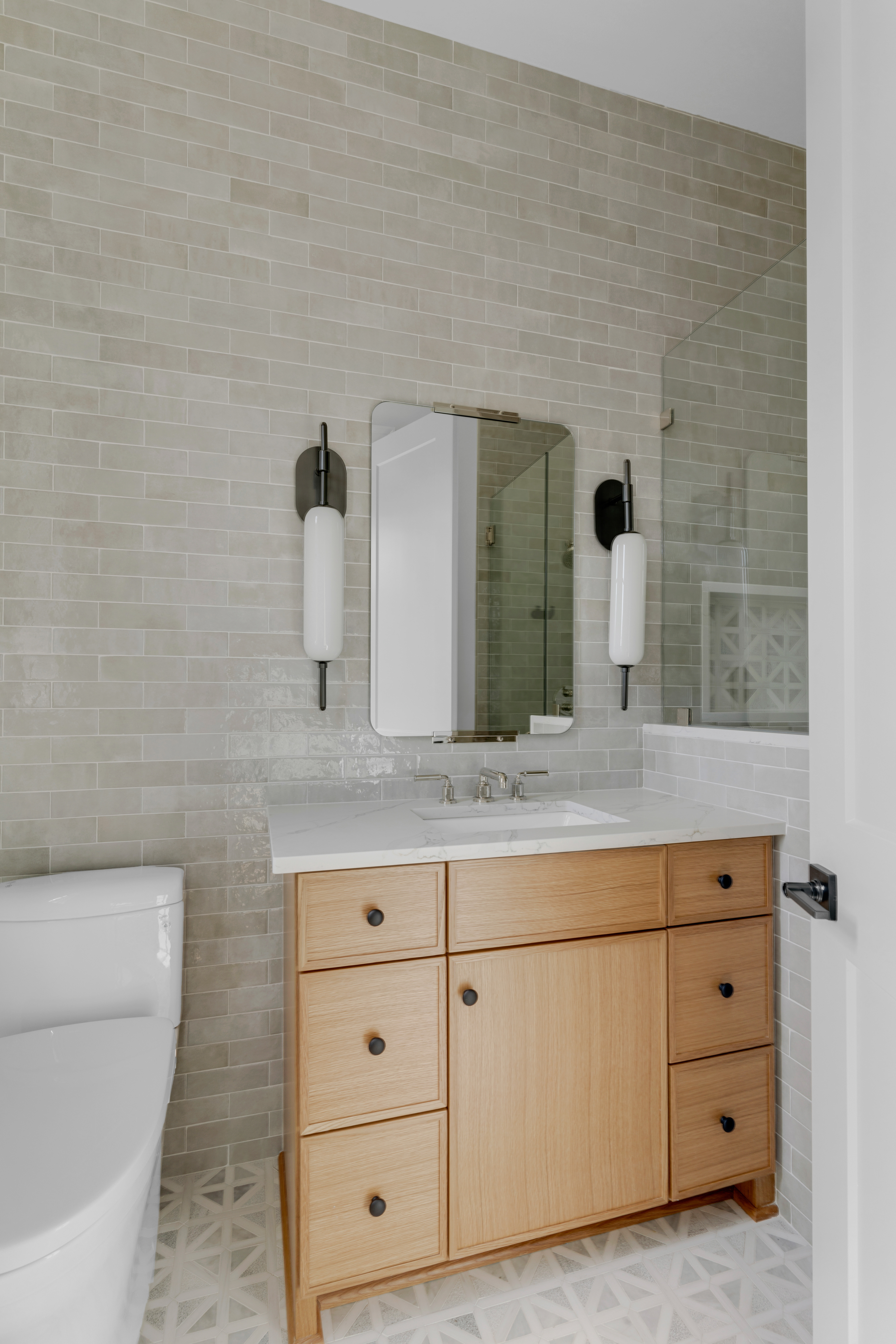 Bathroom with wall paper, light wood vanity, mirror and sconces