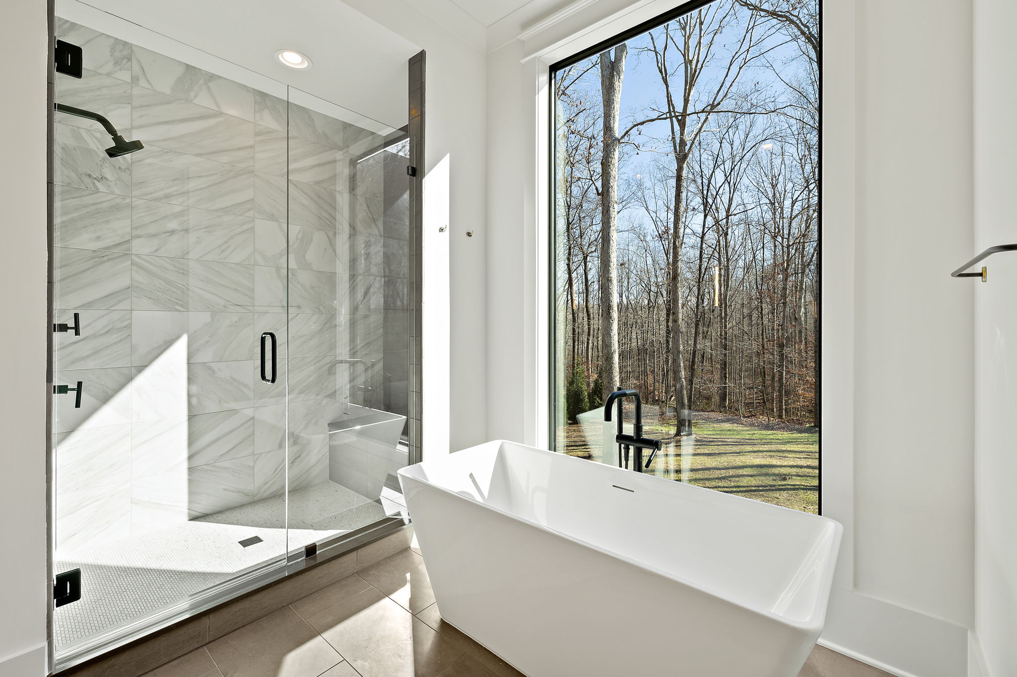 View of tub in front of a large window with a walk-in shower with gold shower head