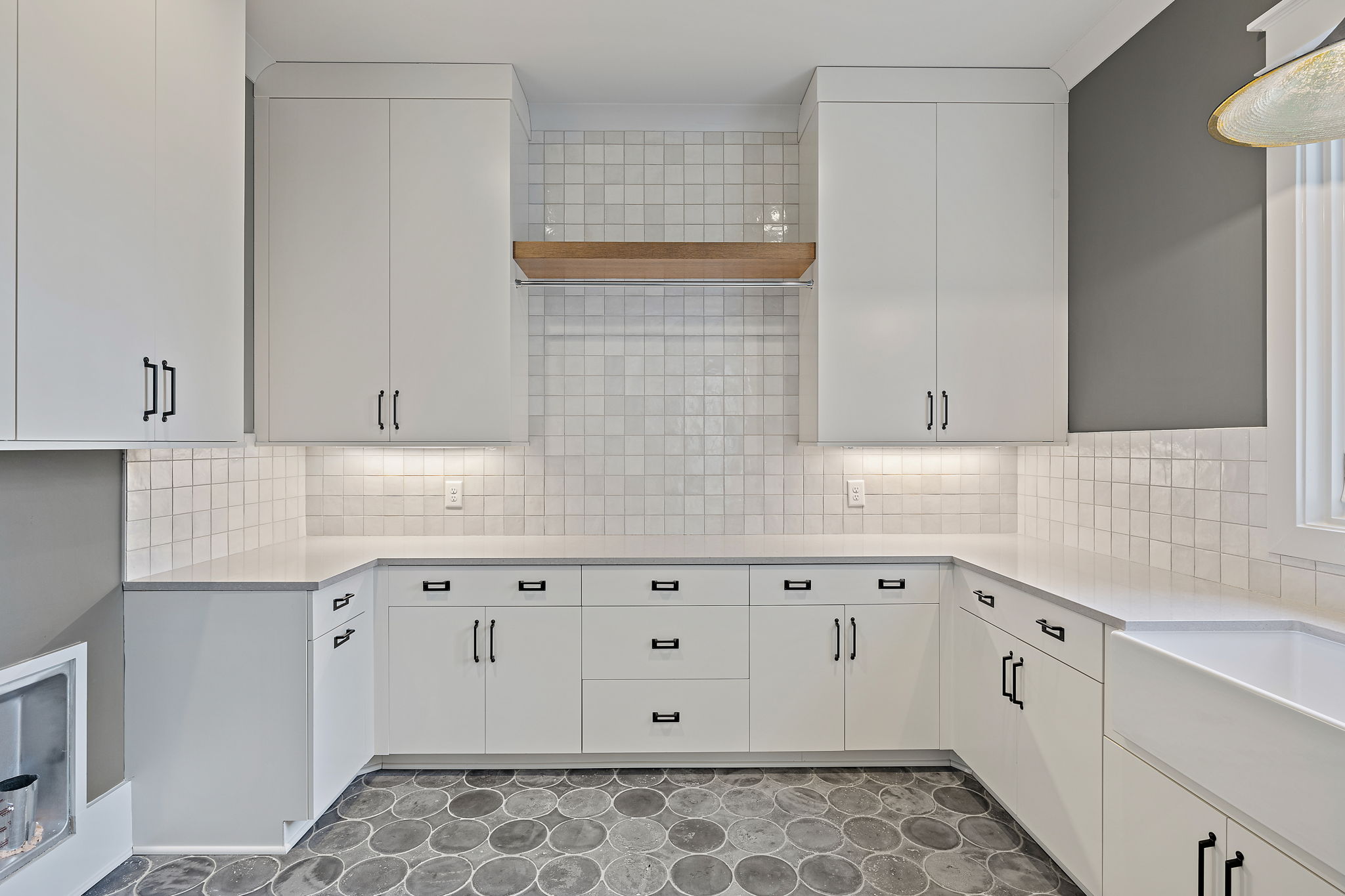 Laundry room with white cabinets and countertops, a single window, light gray walls and gray circular tile flooring