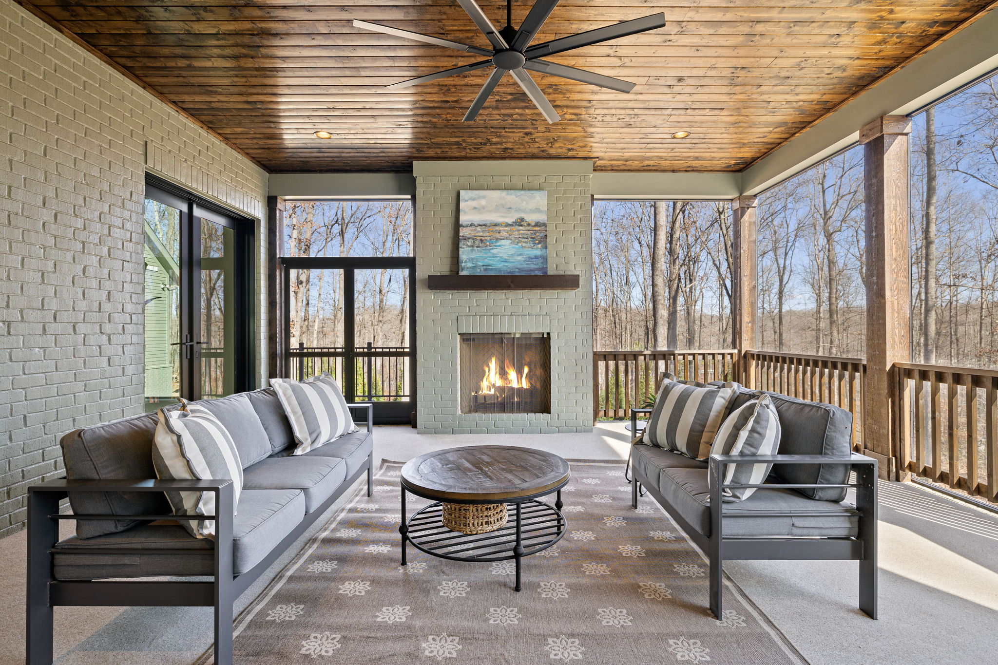 Furnished, screened-in back porch with fireplace and wood stained ceiling with ceiling fan overlooking treefilled lawn