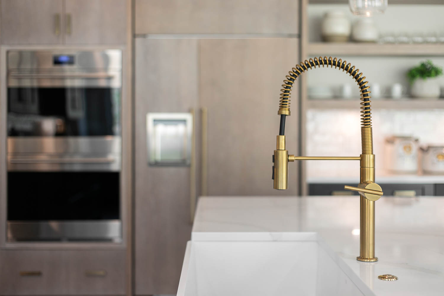 Brushed gold kitchen faucet with light wood stained panel for refridgerator and double oven