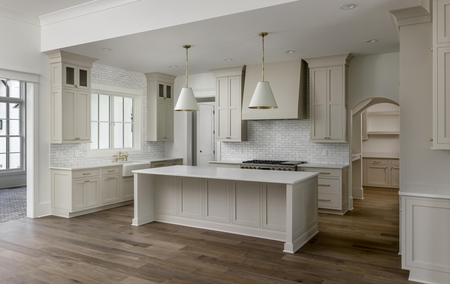 Beige kitchen cabinets with interior window over the sink and white shaded pendant lights