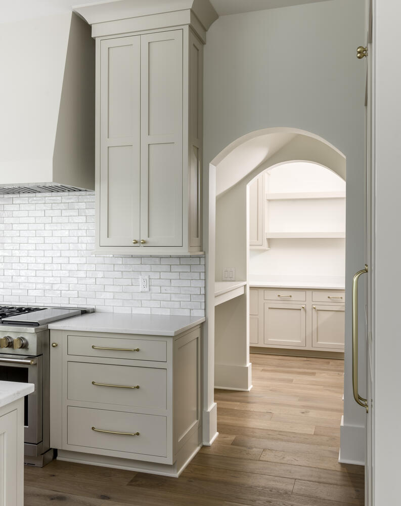Beige kitchen cabinets with kitchen range and arched opening leading into the pantry