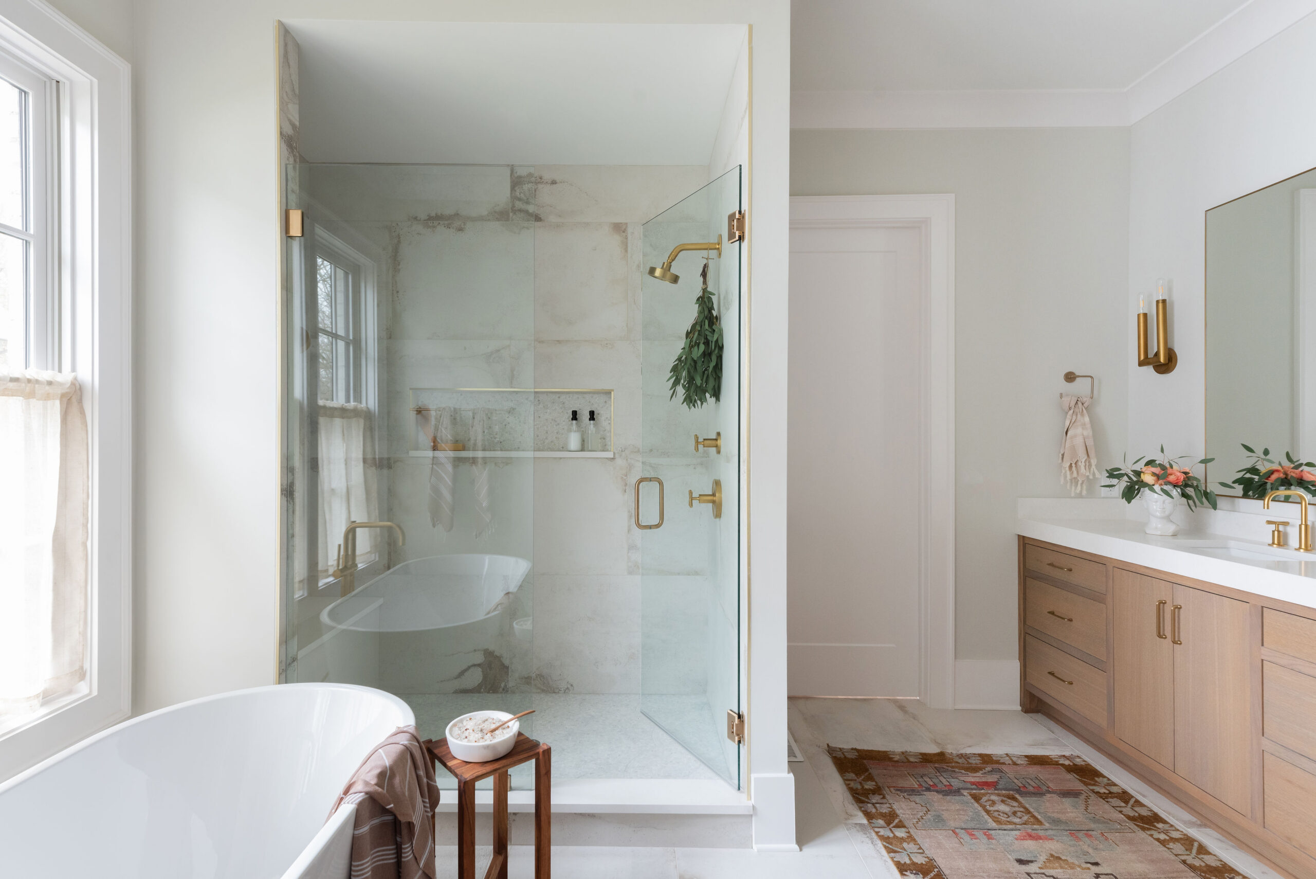 View of tub and floating wood vanity with a walk-in shower with gold shower head and built-in rectangular niche