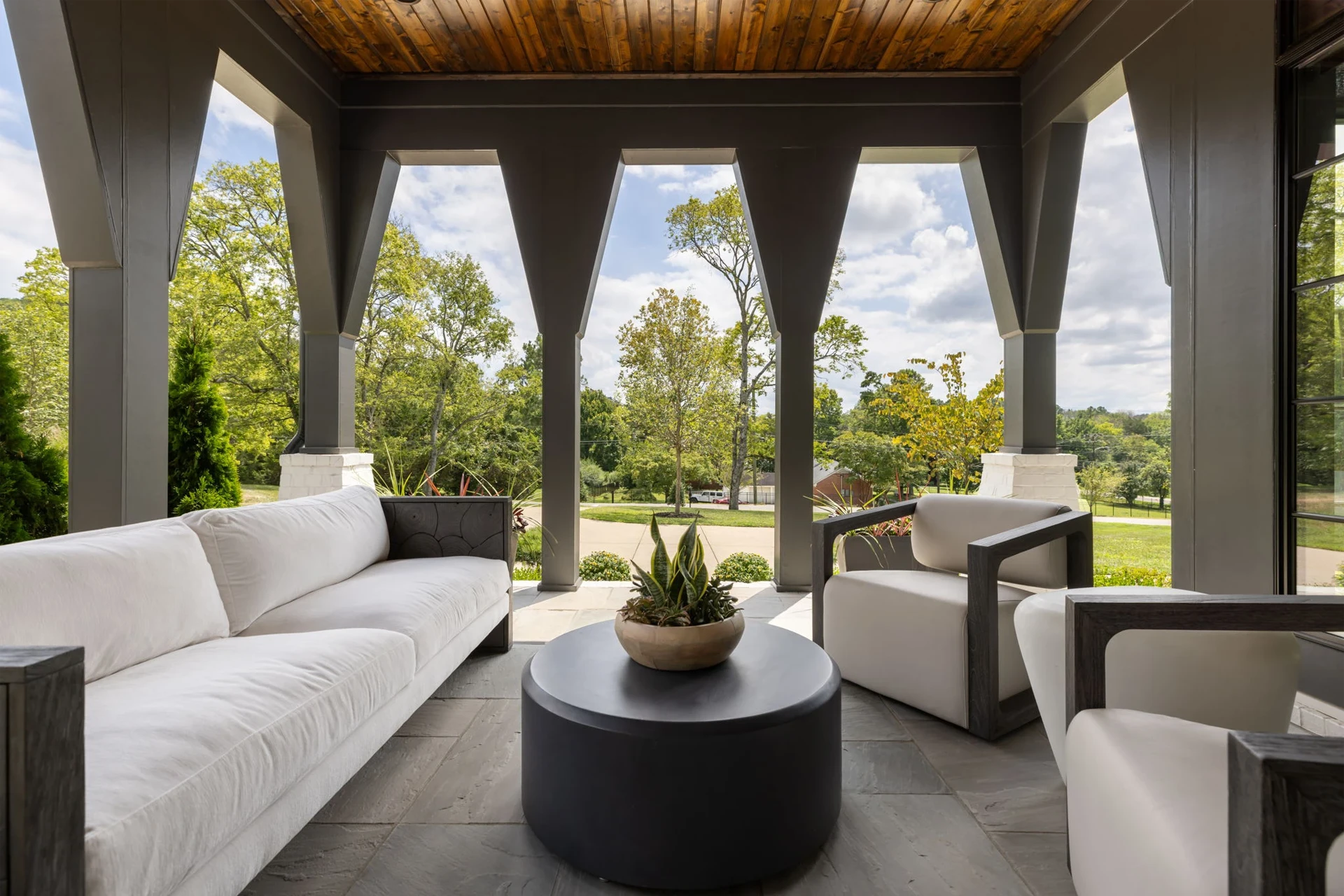 Covered patio with columns, white sofa and armchairs, round black coffee table, and green lawn views