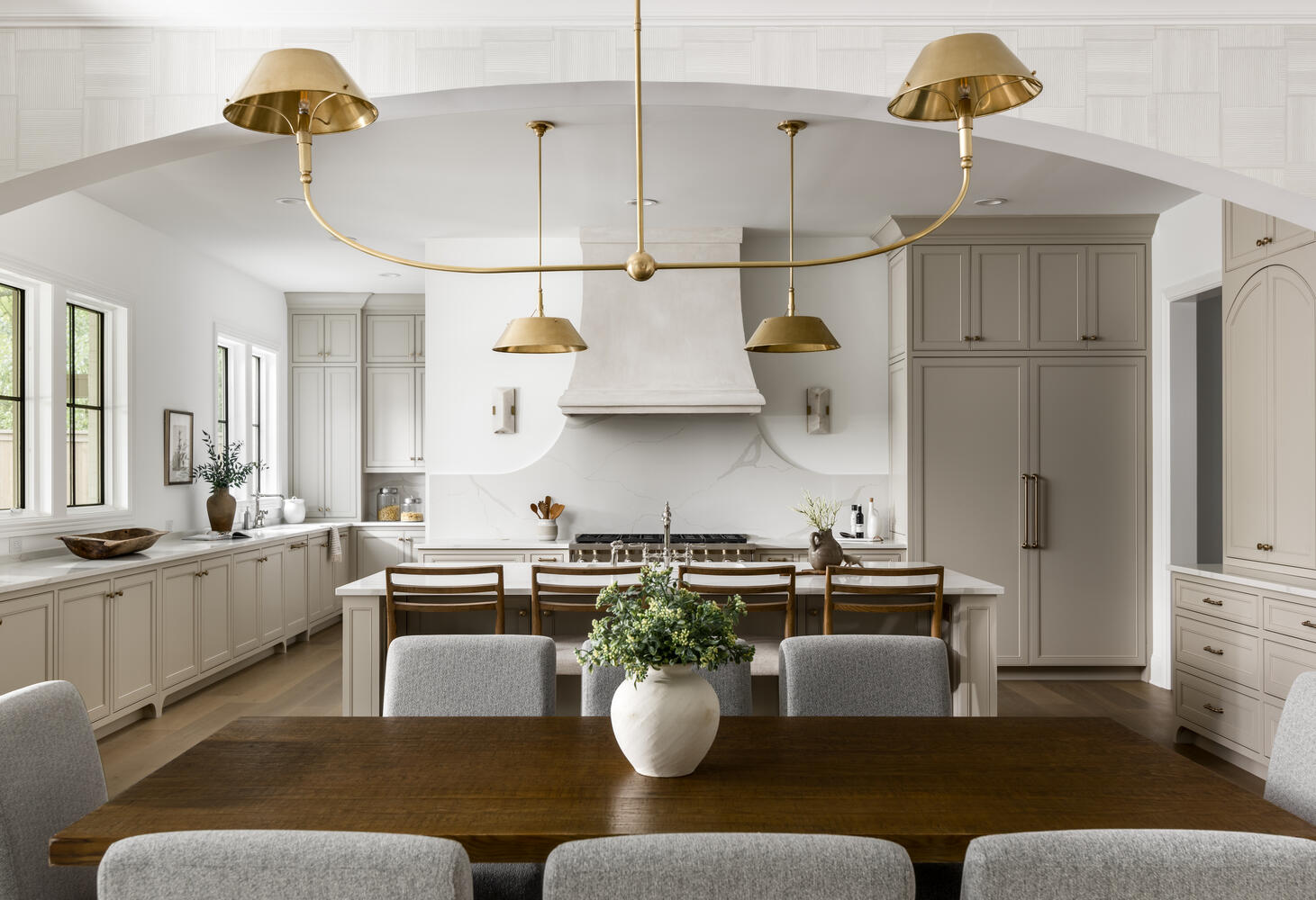 View of kitchen with light greige kitchen cabinets with light countertops and hood with range and kitchen table with gold simple chandelier
