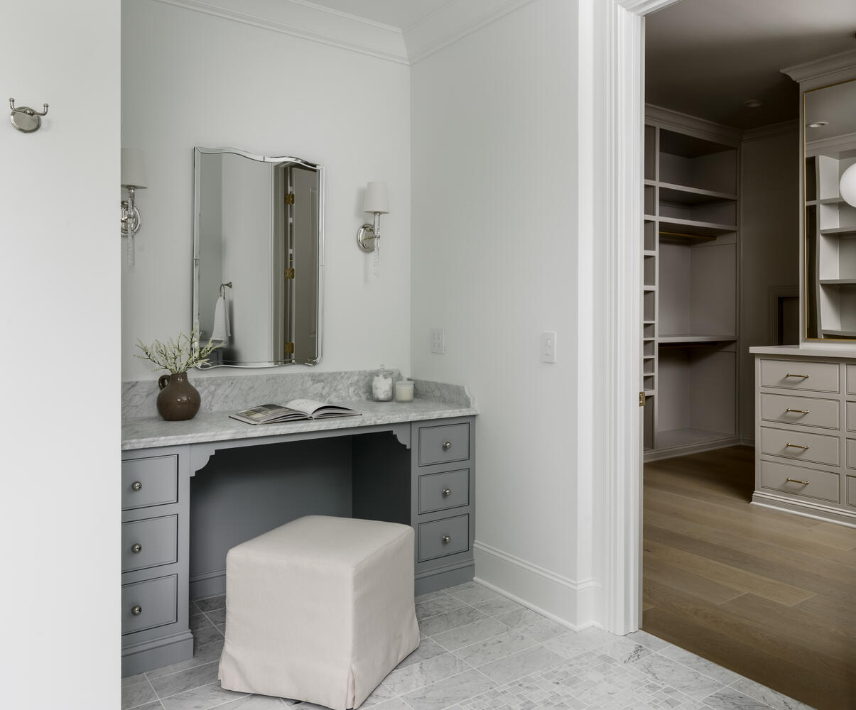 Powder blue vanity with upholstered linen stool with a mirror and sconces and view of closet