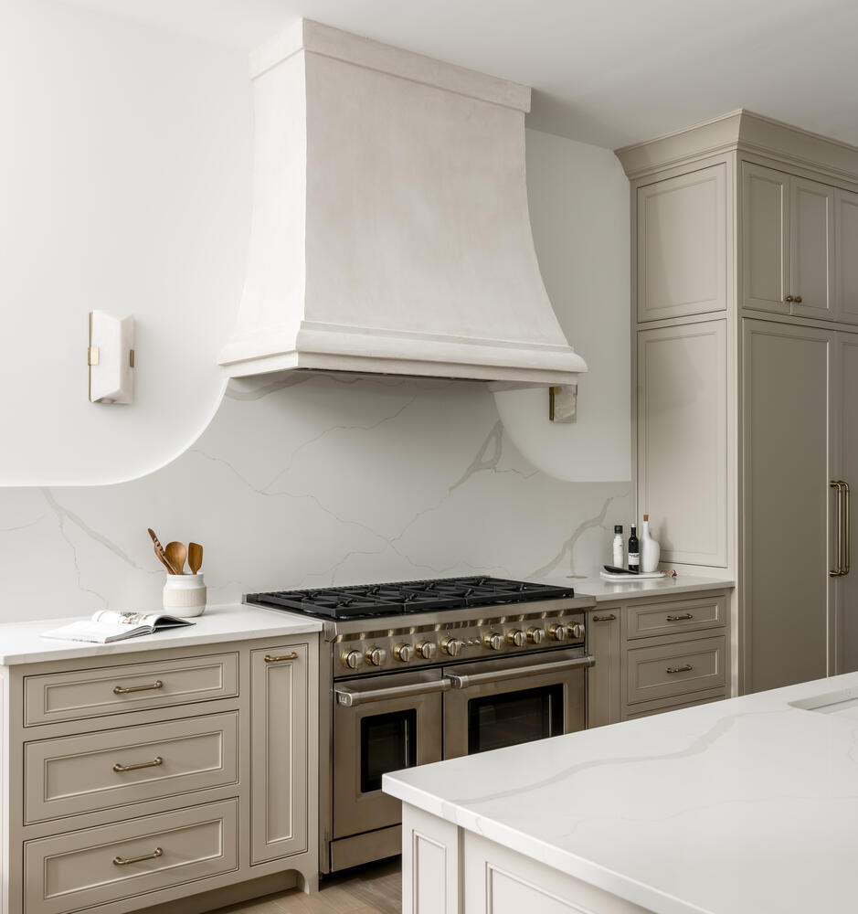 Light greige kitchen cabinets with light countertops and hood with range