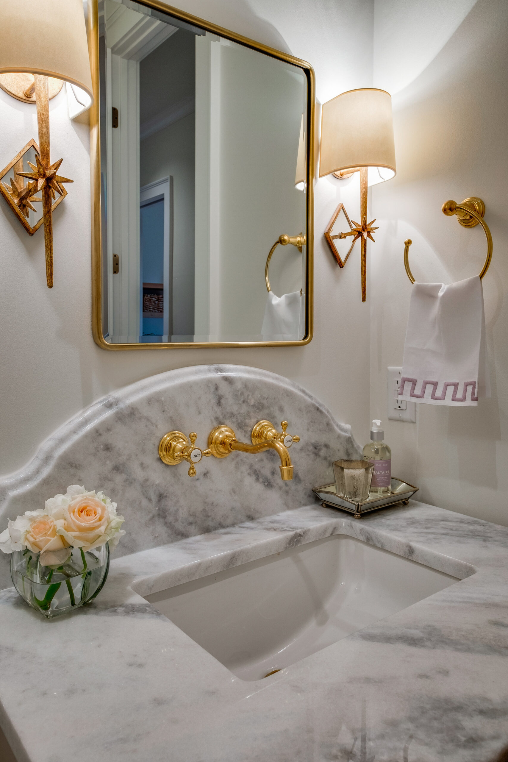 Powder bathroom with marble countertop, a mirror, and sconces