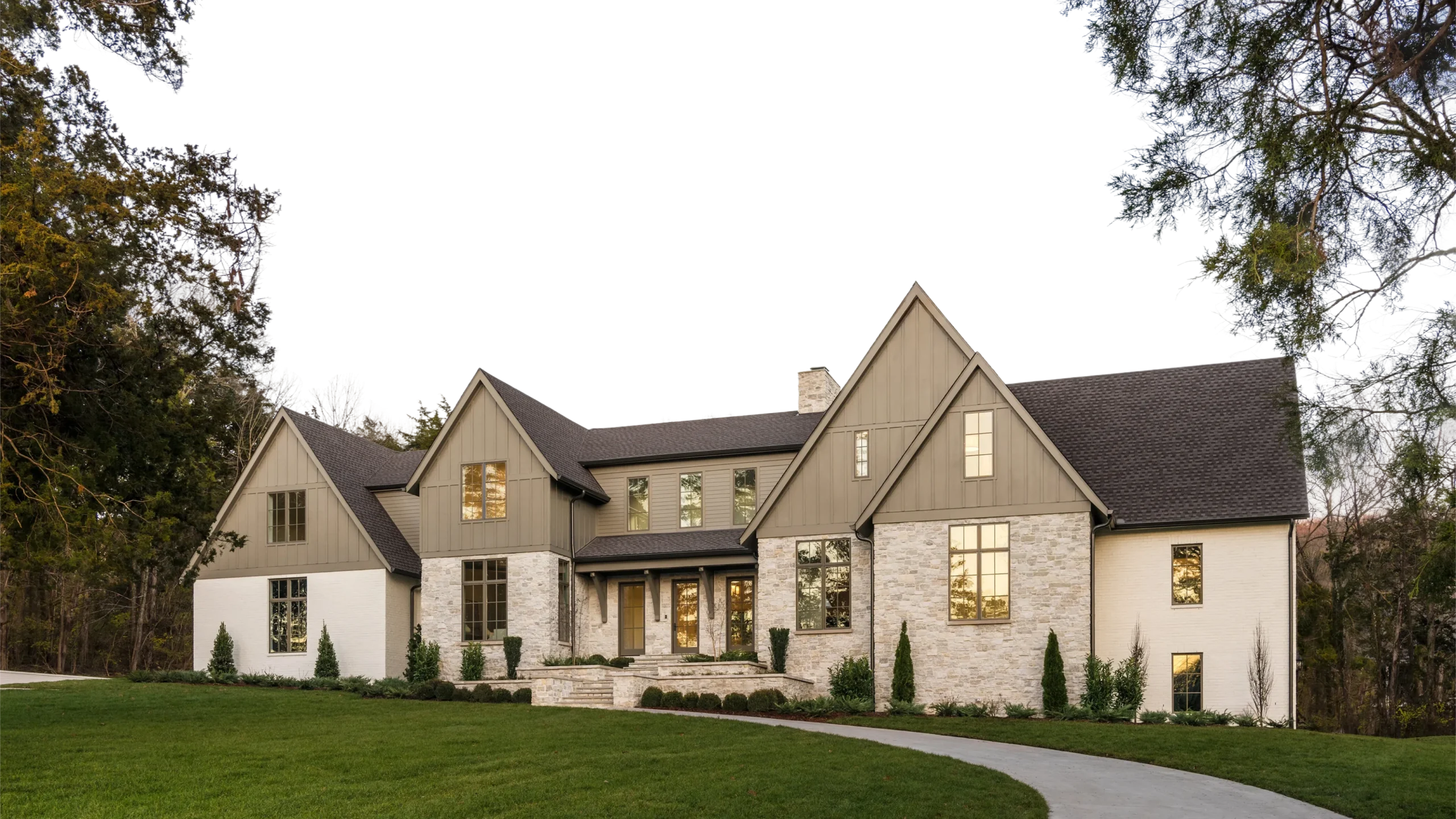 Two-story custom home with stone and board-and-batten siding, dark gable roof, and manicured front lawn