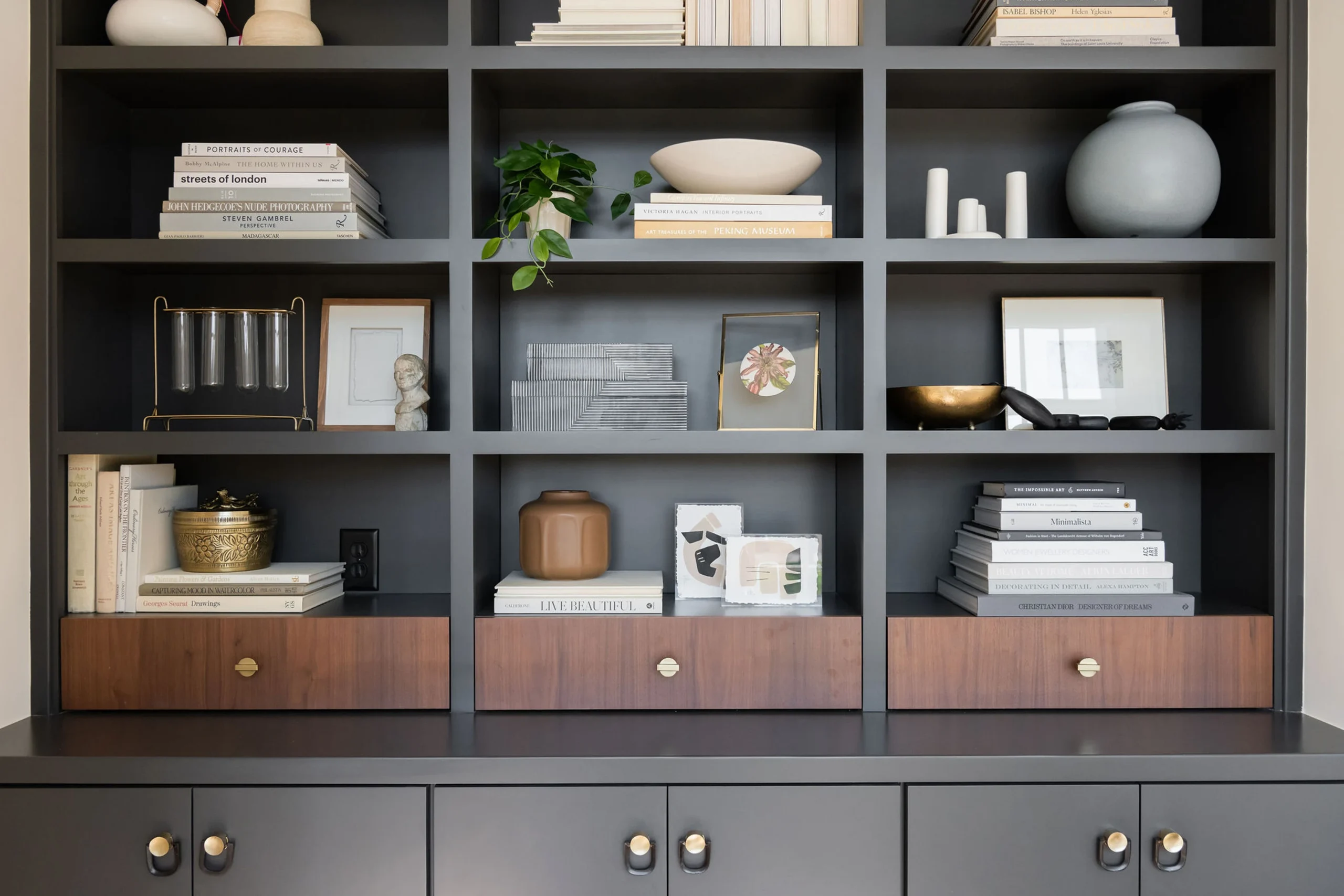 Styled dark built-in shelving with books, decorative objects, a plant, and walnut drawers