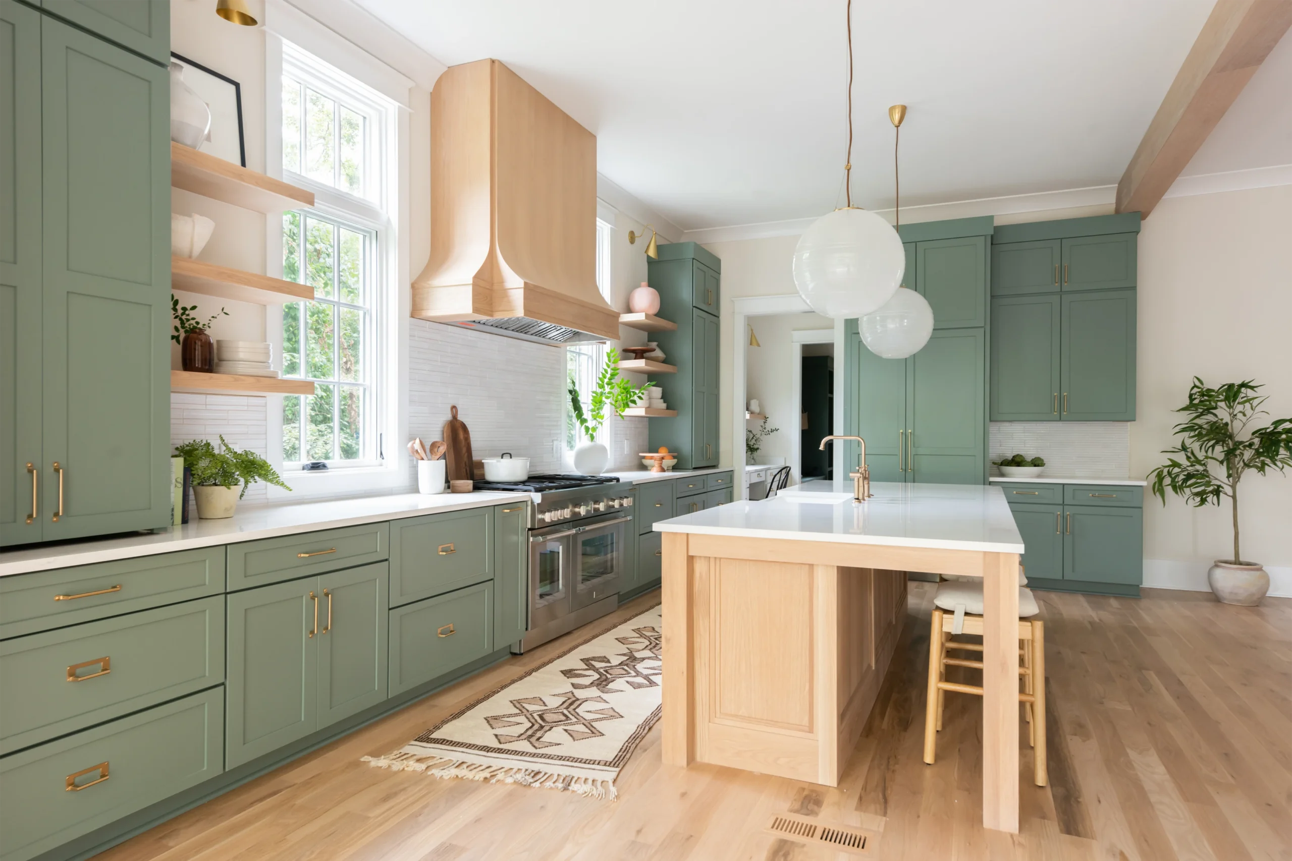 Green kitchen with natural wood range hood and island, open shelving, and globe pendant lights