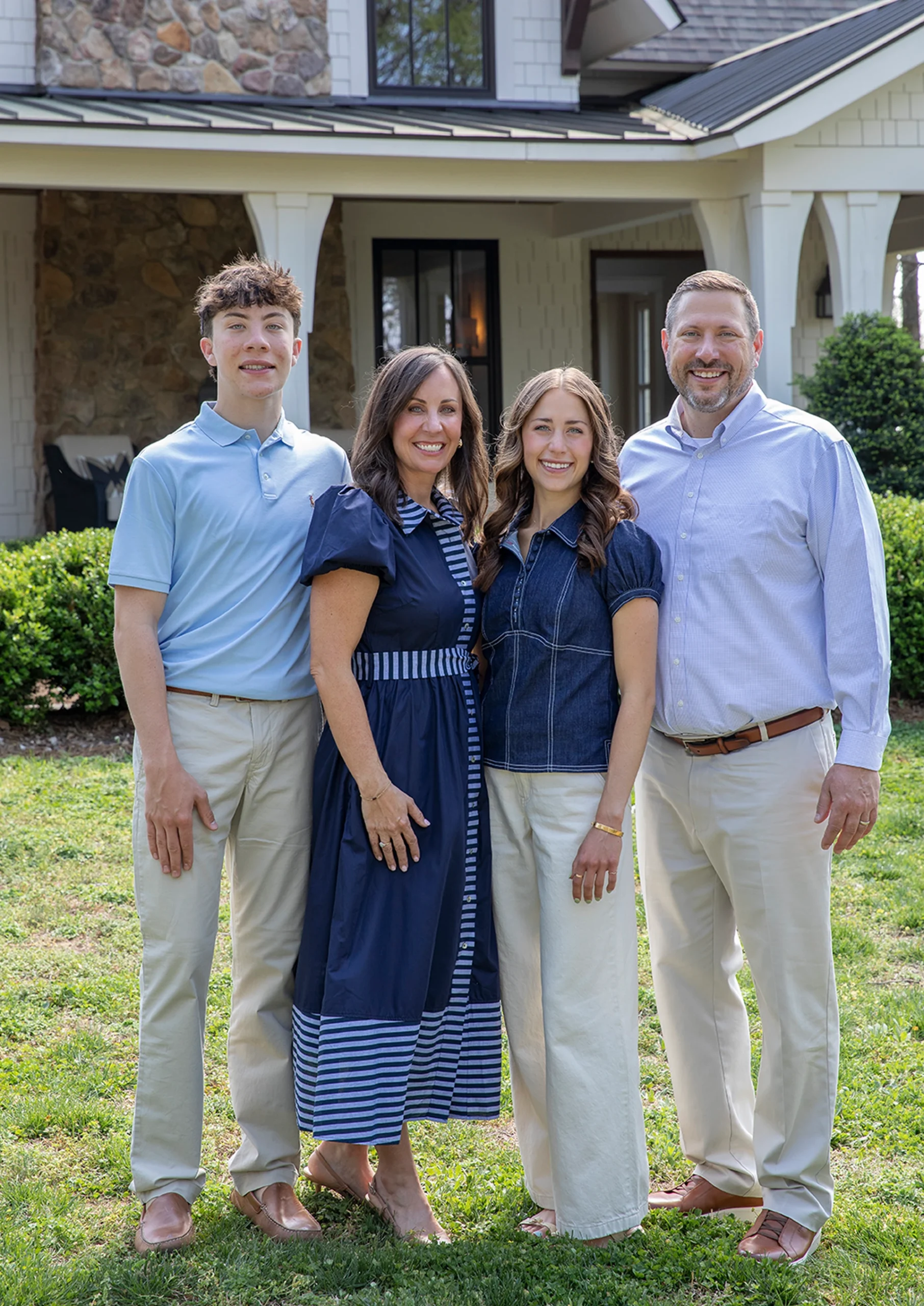 Family of four in blue and white attire smiling in front of a finished home