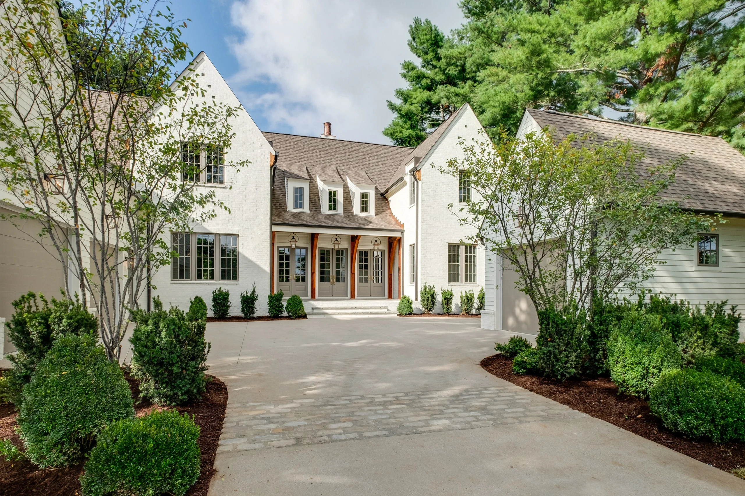 White home with dark hipped roof, glass French entry doors, and a landscaped paver driveway