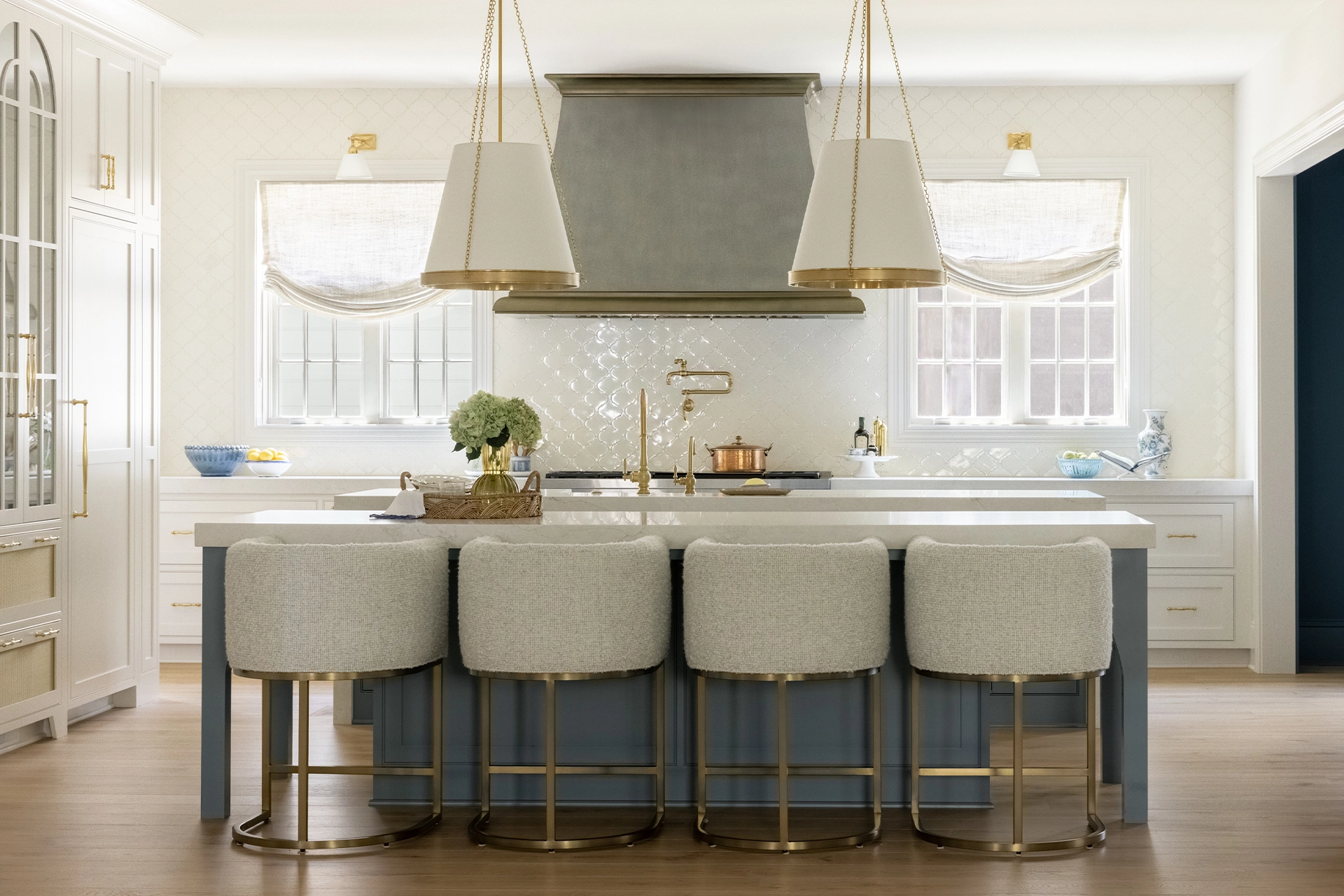 Kitchen with blue island, boucle counter stools, upholstered range hood, and brass accents