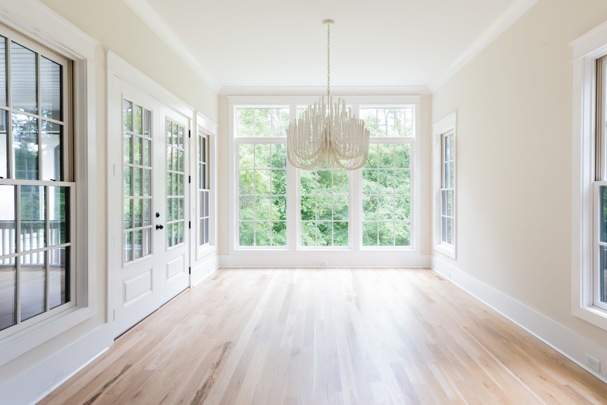 Dining area with white fluted chandelier, white walls, and large, floor to ceiling white grid windows