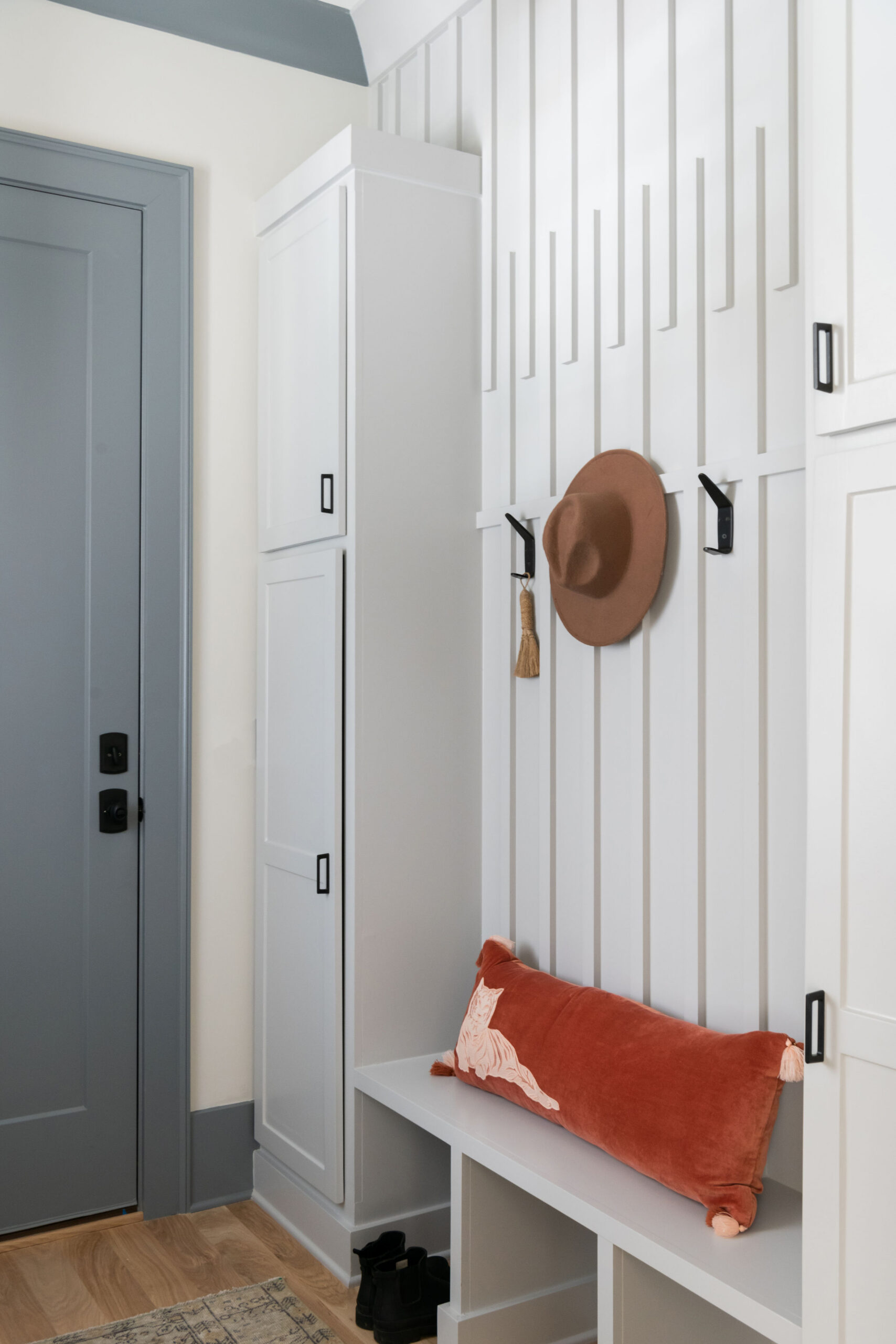 Creamy white mudbench with black hooks and a bench with open storage below bench with modern paneling