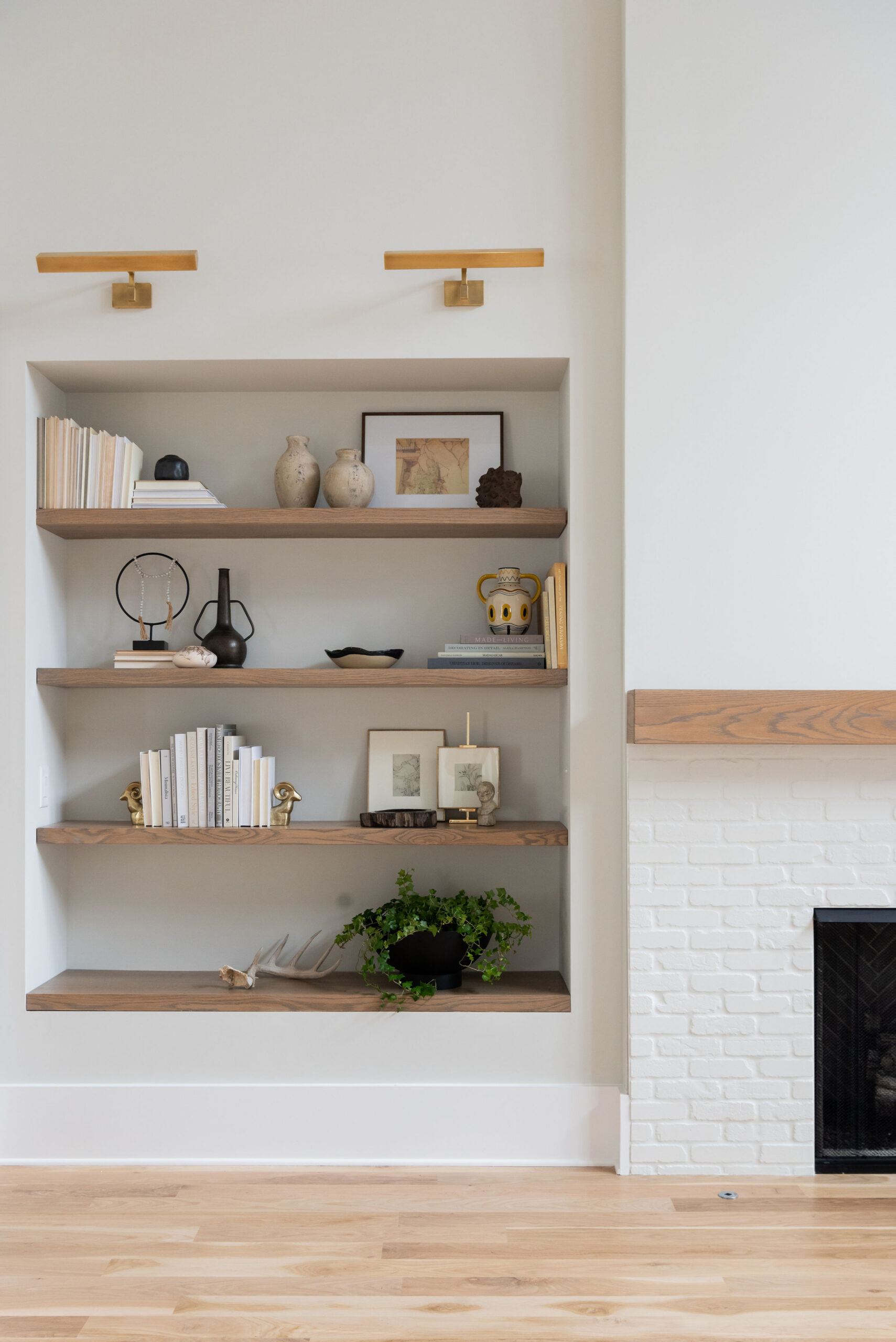 White walls with built in, natural wood stained shelving with sconce lighting and view of fireplace