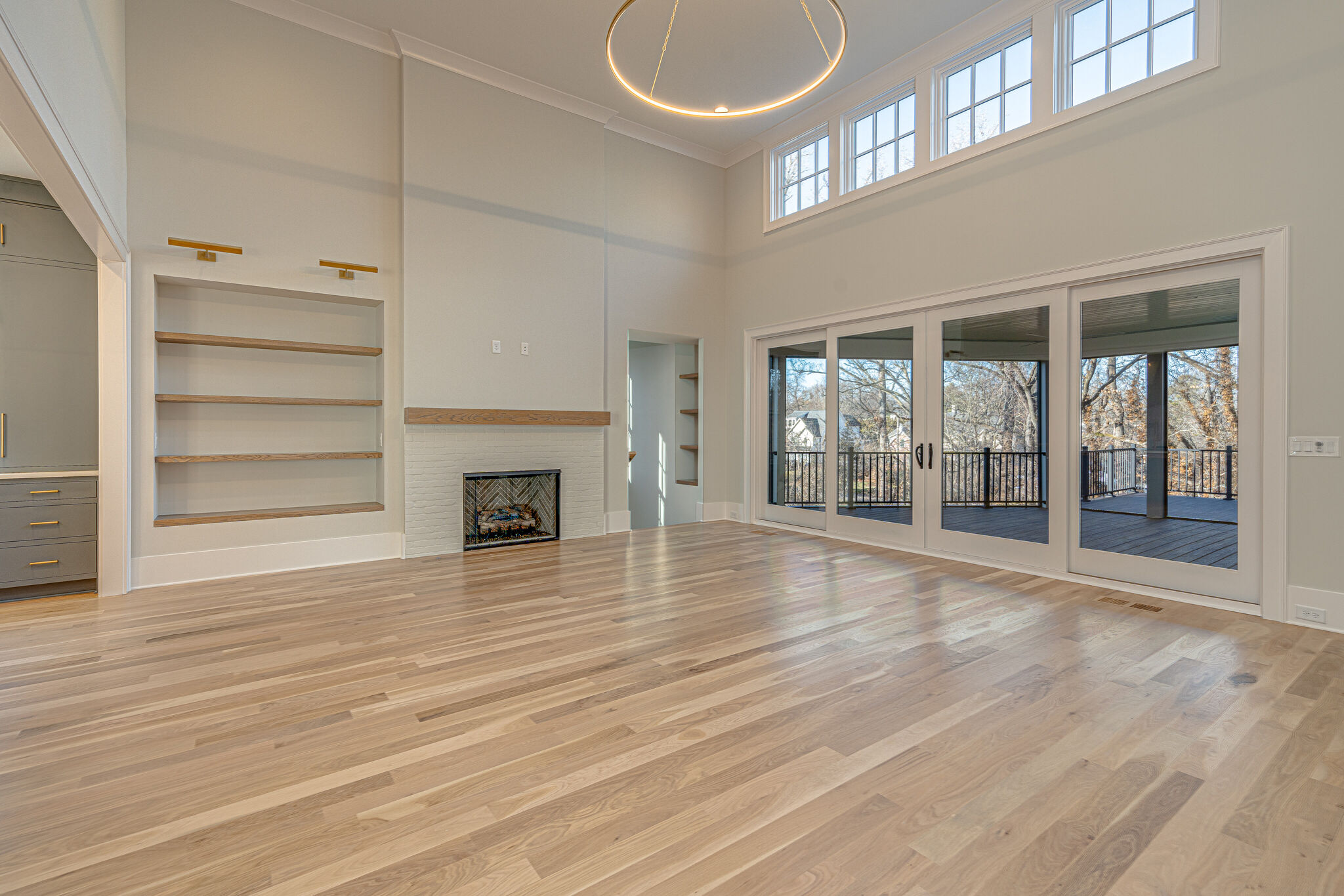 High ceiling family room with white walls with built in, natural wood stained shelving with sconce lighting, a view of the fireplace, a circular chandelier, and large windows