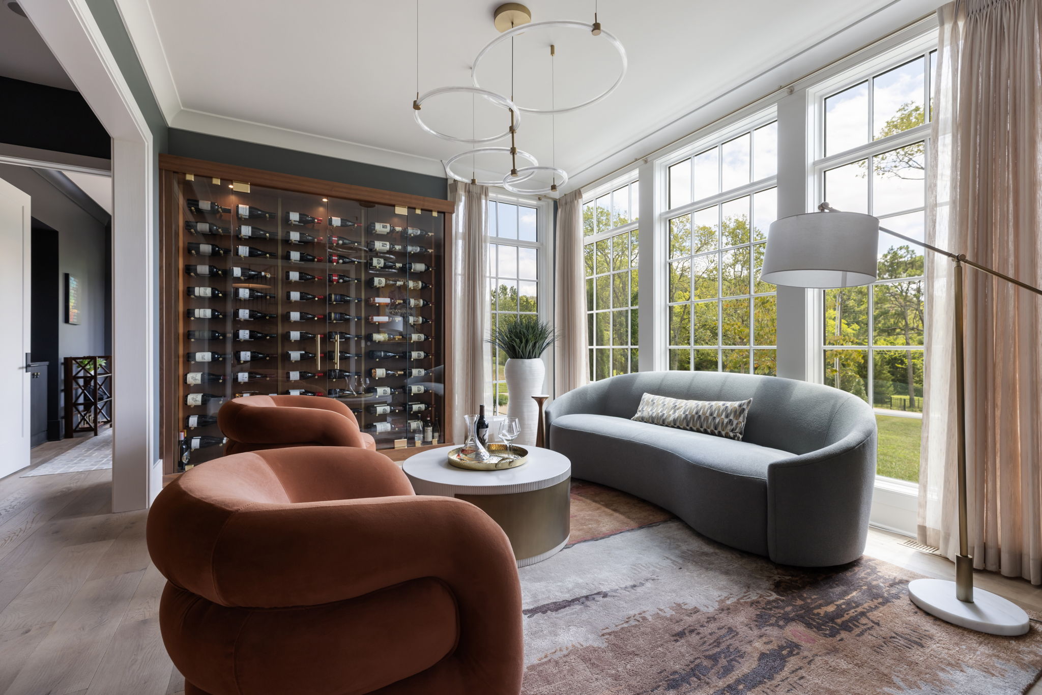Sitting room complete with modern furniture and coffee table with a large wall of floor to ceiling windows and a glass enclosed wine cabinet
