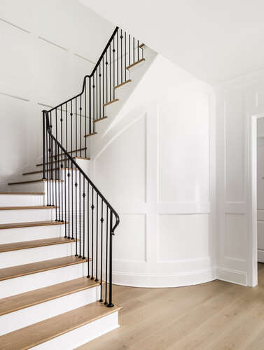 White paneled stairway black iron spindles with a curved paneled wall at the base of the steps